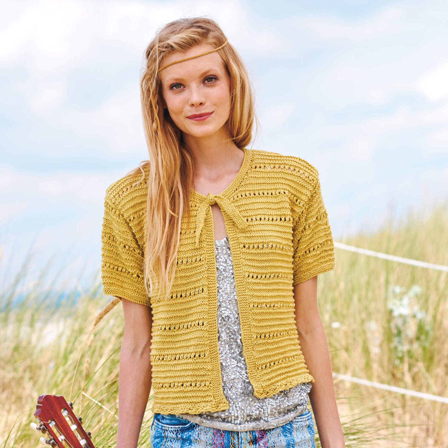 Strickanleitung Jacke mit Lochmuster aus Mille Fili: Frau trägt gelbe, kurzärmelige Jacke am Strand.