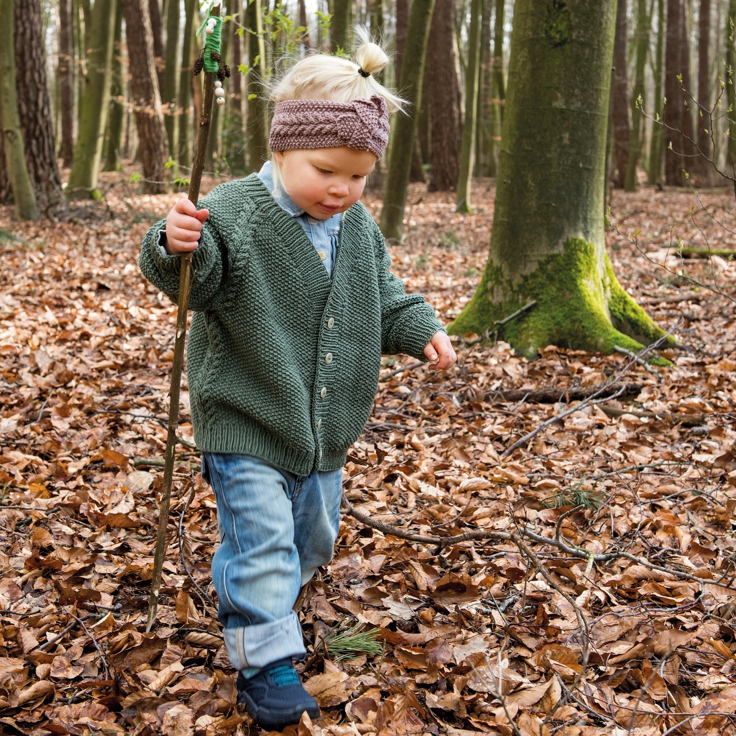 Strickanleitung Kinderjacke und Stirnband: Kind im Wald mit grüner Jacke und Stirnband aus Merino.