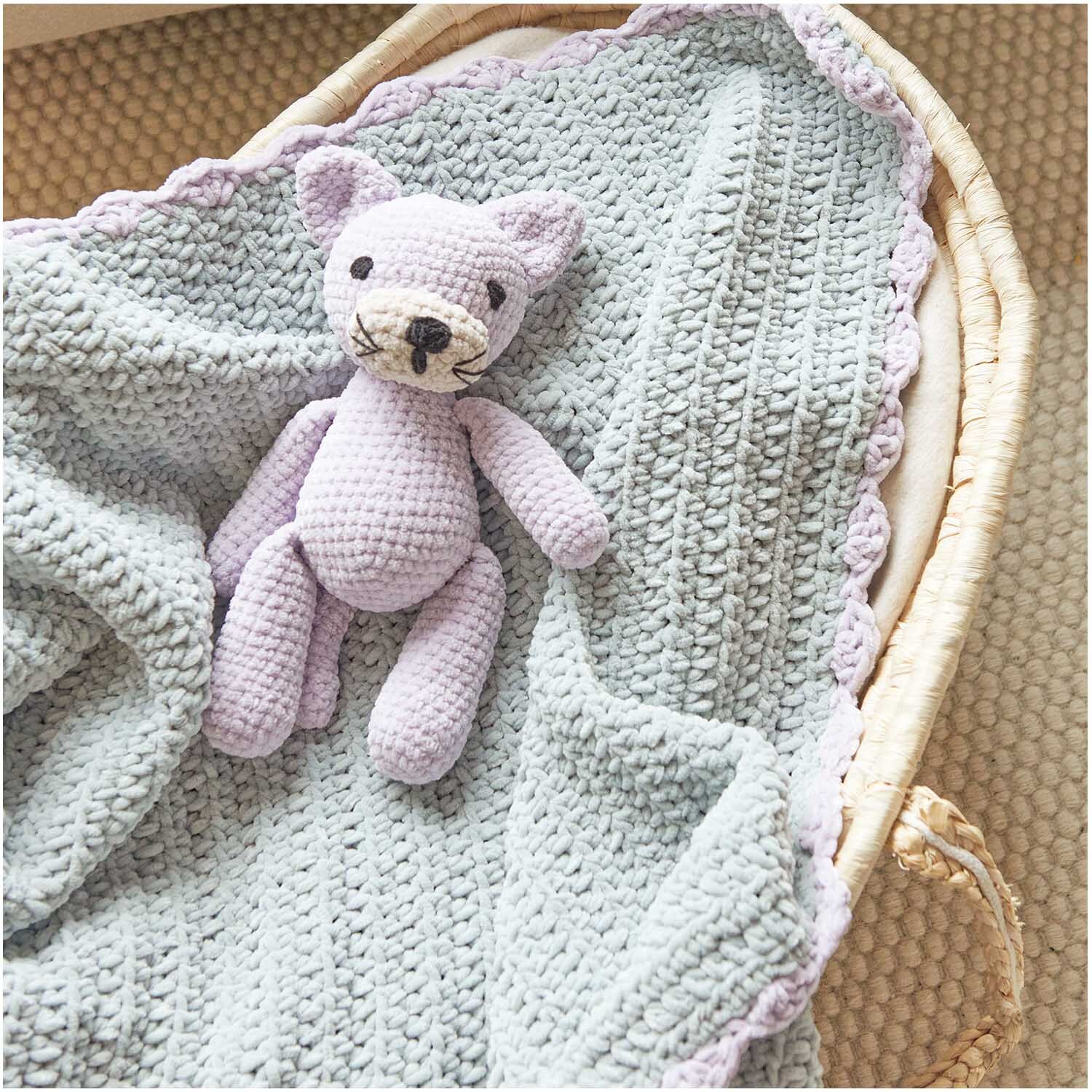 Häkelset Katze Modell 14 aus Baby Chenillove: Lila gehäkelte Katze auf pastellgrüner Decke in einem Korb.