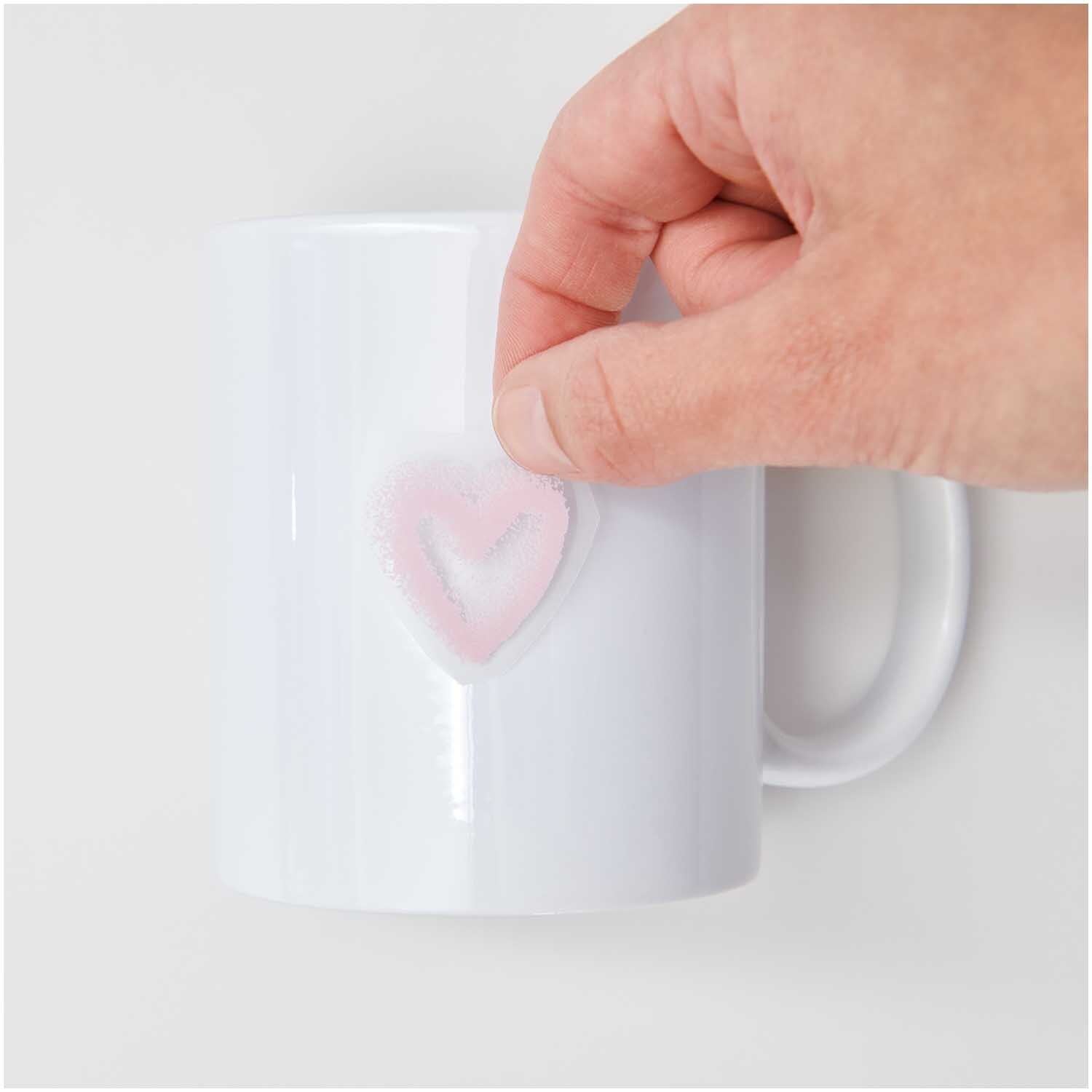 Transfermotiv Spray Herzen: Eine Hand platziert ein rosa Herz auf einer weißen Tasse. 12 Stück von Rico Design.