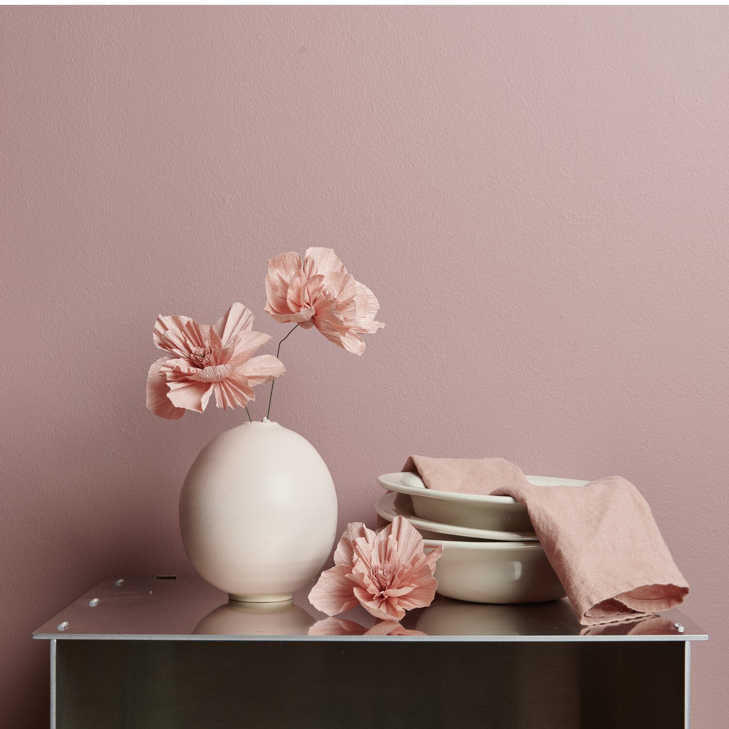 Krepppapier Blüten in einem eleganten Arrangement mit Vasen und Geschirr auf einem Tisch.