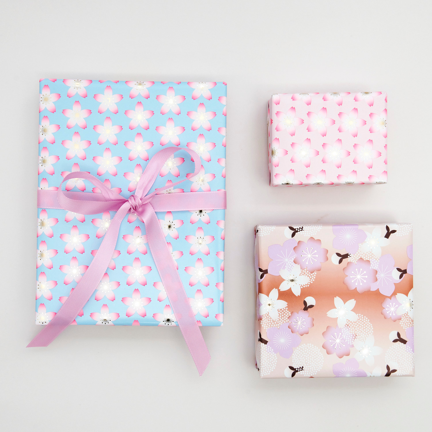 Geschenkpapier Kirschblüten Pink: Drei Geschenke mit Kirschblütenmuster in Rosa, Blau und Orange, verpackt mit Rico Design Papier.