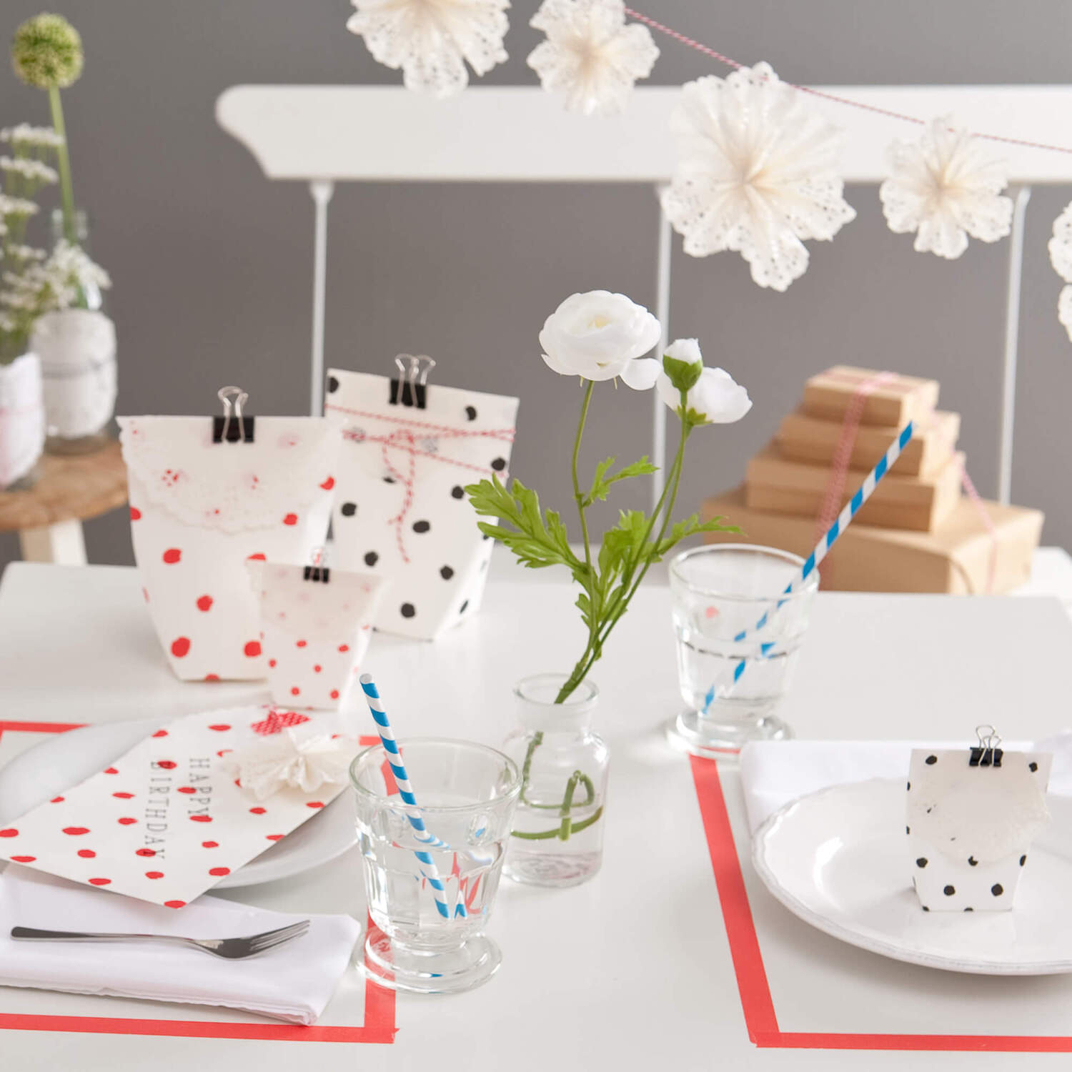 Bastelanleitung Dekorieren mit Tortenspitze: Tisch mit dekorativen Papierblumen und gepunkteten Tüten.