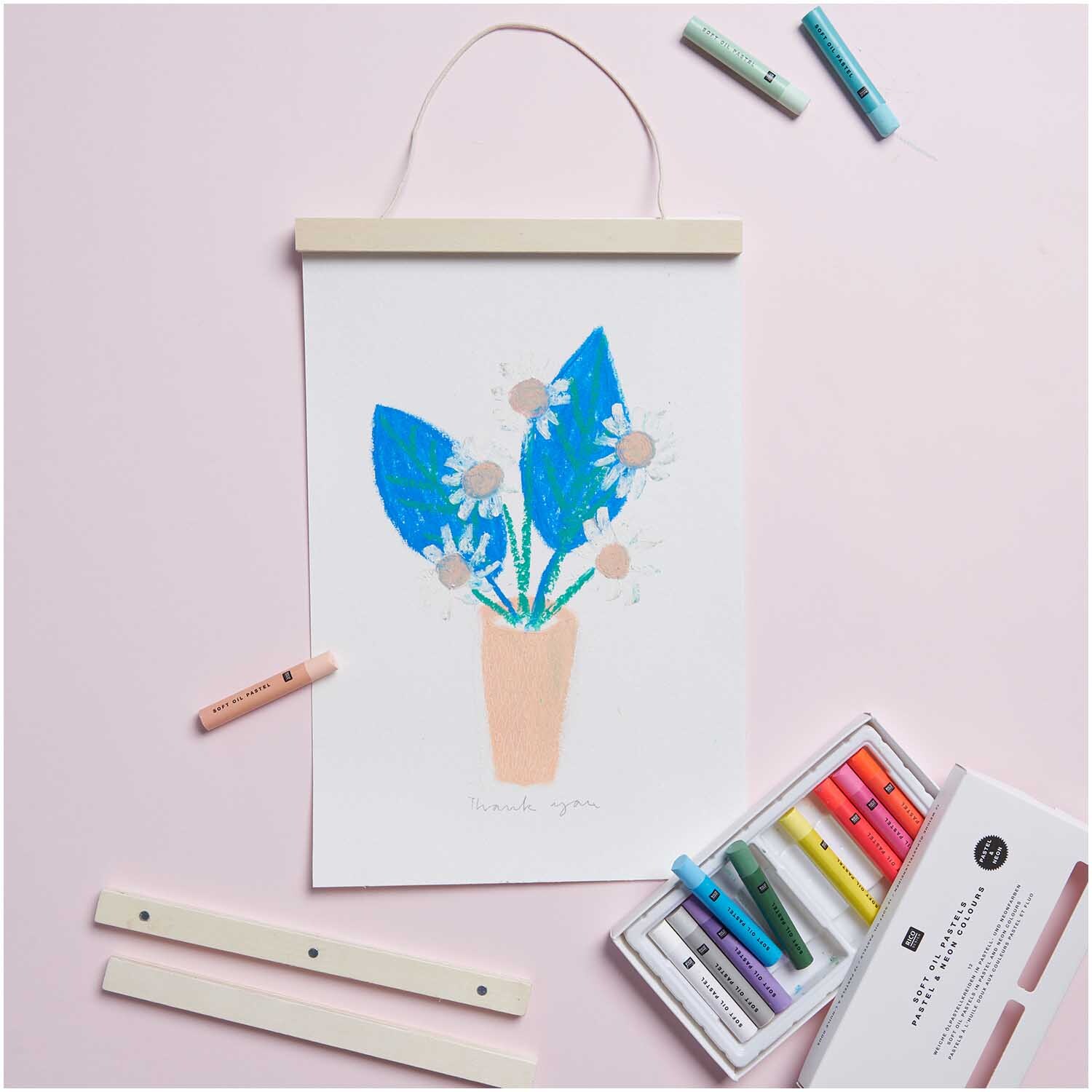 Ölpastellkreide Pastell & Neon 12 Farben von Rico Design, mit Zeichnung von Blumen in Blau und Rosa auf rosa Hintergrund.