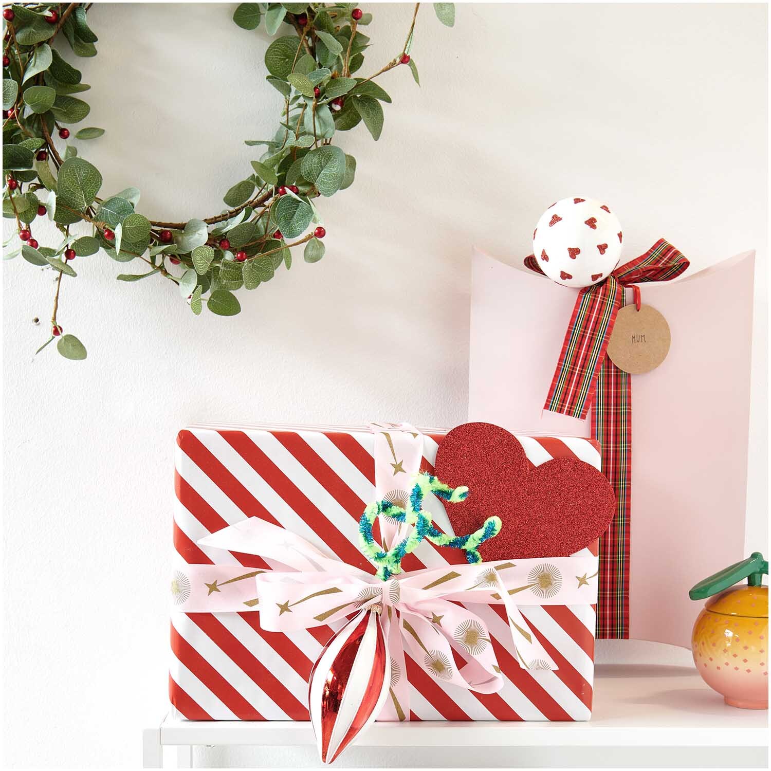 Filz Untersetzer Herzen rot 15x12,9cm 6 Stück von Rico Design. Geschenkverpackung mit Herzmotiv und dekorativem Kranz im Hintergrund.