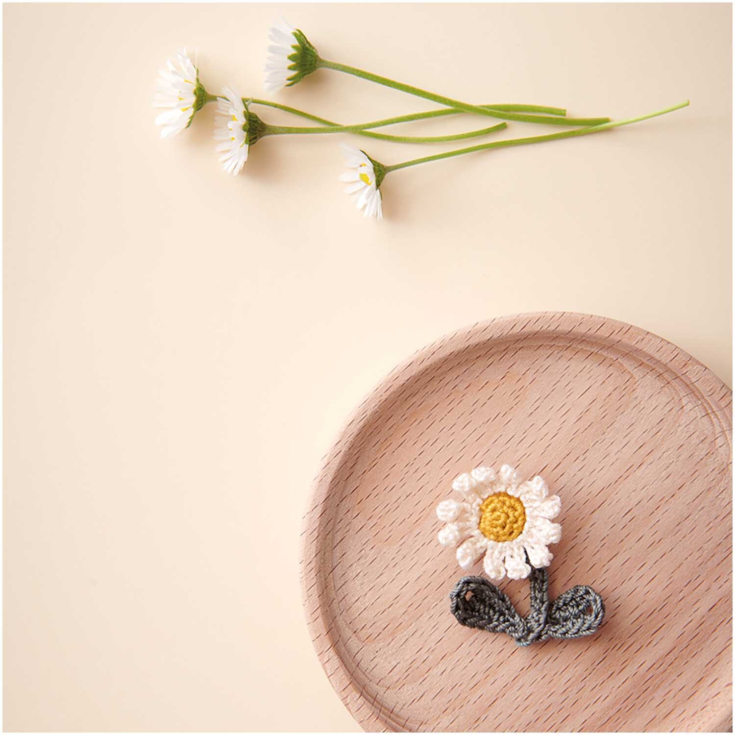 Essentials Crochet: Cremefarbenes Garn von Rico Design, dekoriert mit gehäkelter Blume auf Holzplatte.