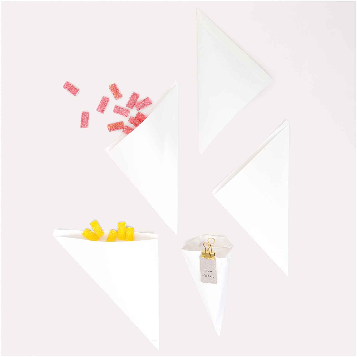 Spitztüten weiß 170x170mm 12 Stück von Rico Design, gefüllt mit bunten Süßigkeiten und Büroklammern.
