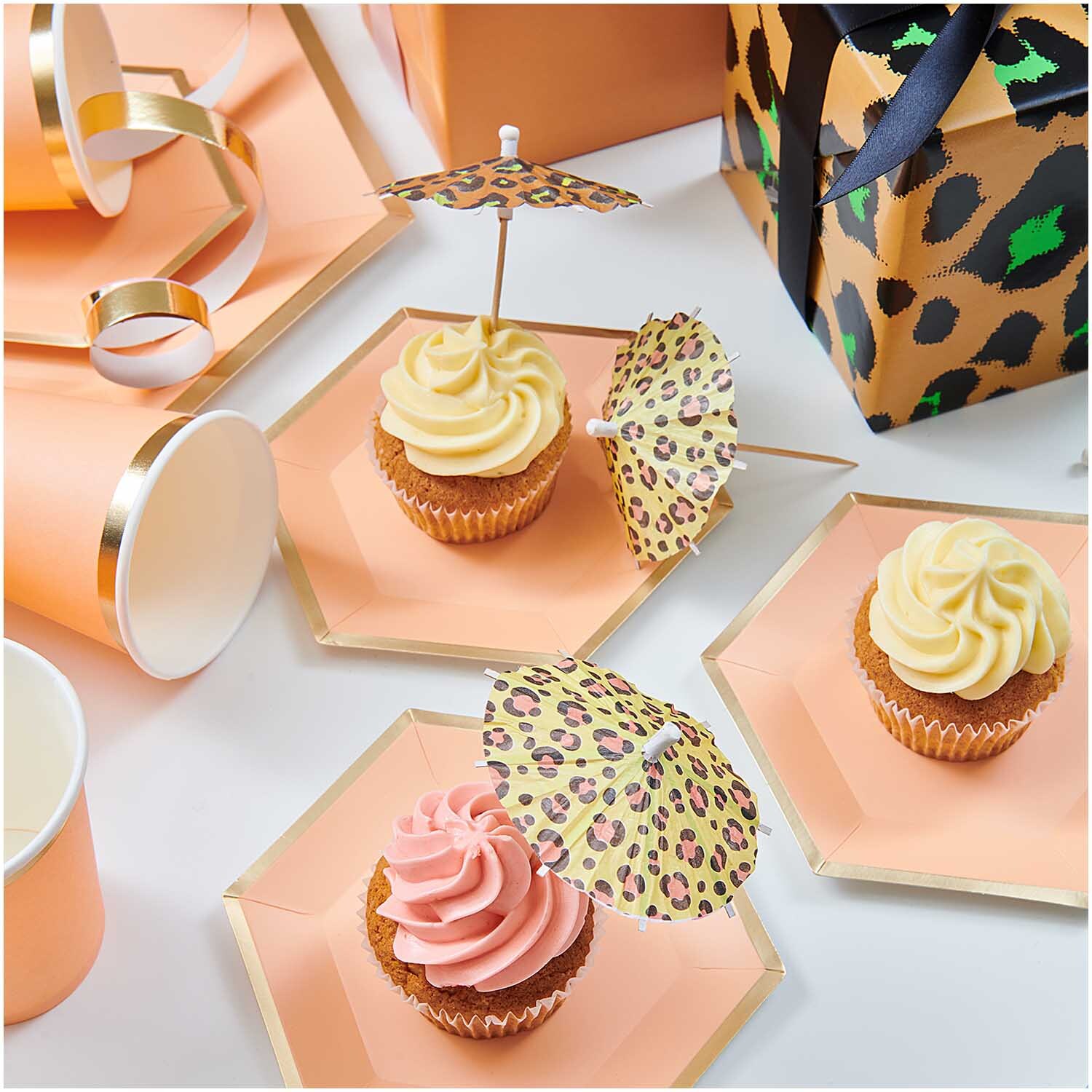 Picker Schirmchen Acid Leo 8,3cm 12 Stück dekorieren Cupcakes auf orangefarbenen Tellern. Die Schirmchen haben ein Leopardenmuster.