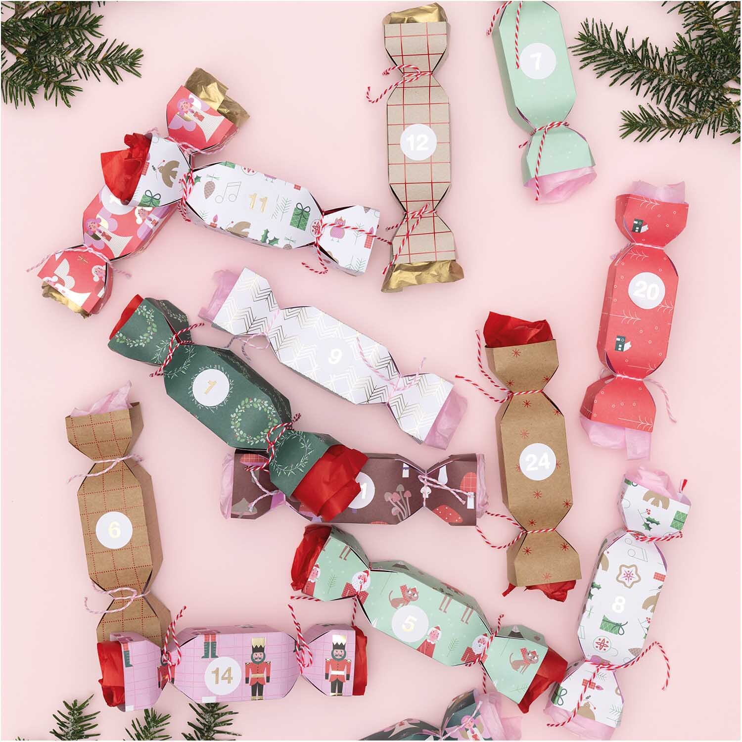 Paper Poetry Motivpapierblock Christmas is in the air: Bunte Weihnachtsknallbonbons auf rosa Hintergrund, dekoriert mit Tannenzweigen.