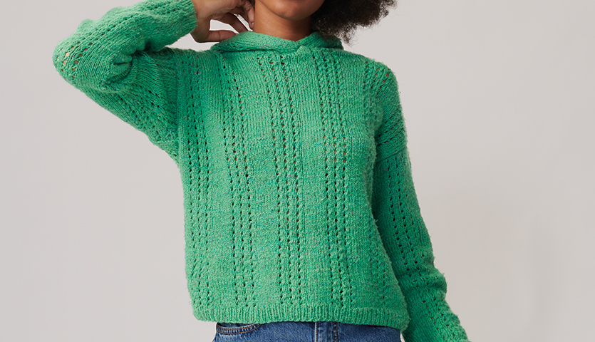 Strickanleitung Hoodie aus Fashion Cottony: Frau trägt grünen gestrickten Hoodie mit Kapuze, ideal für Freizeitkleidung.