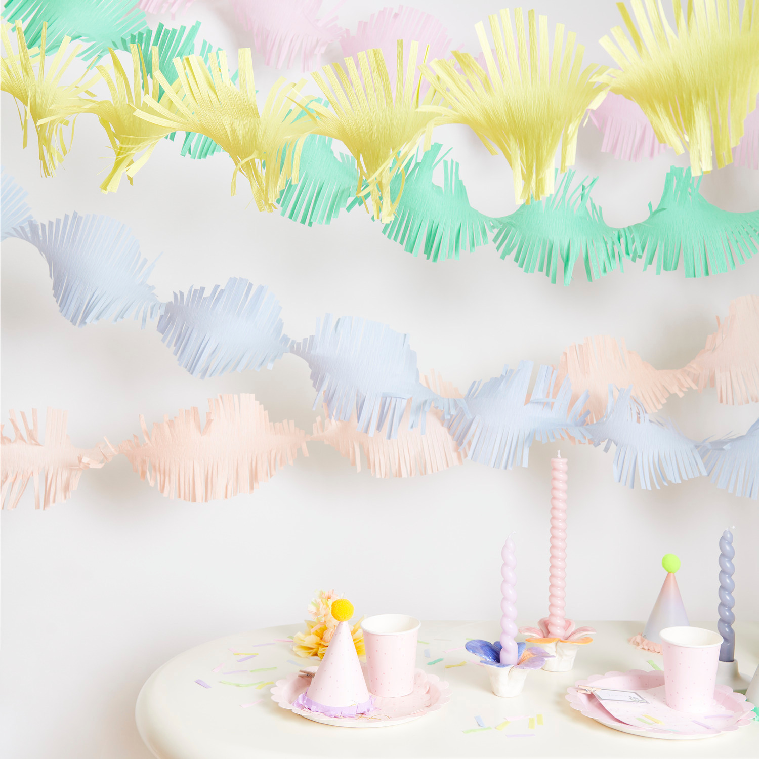 Krepp-Girlande gedreht Regenbogen Pastell Mix dekoriert einen Tisch mit Partyzubehör in sanften Pastellfarben. Ideal für festliche Anlässe.