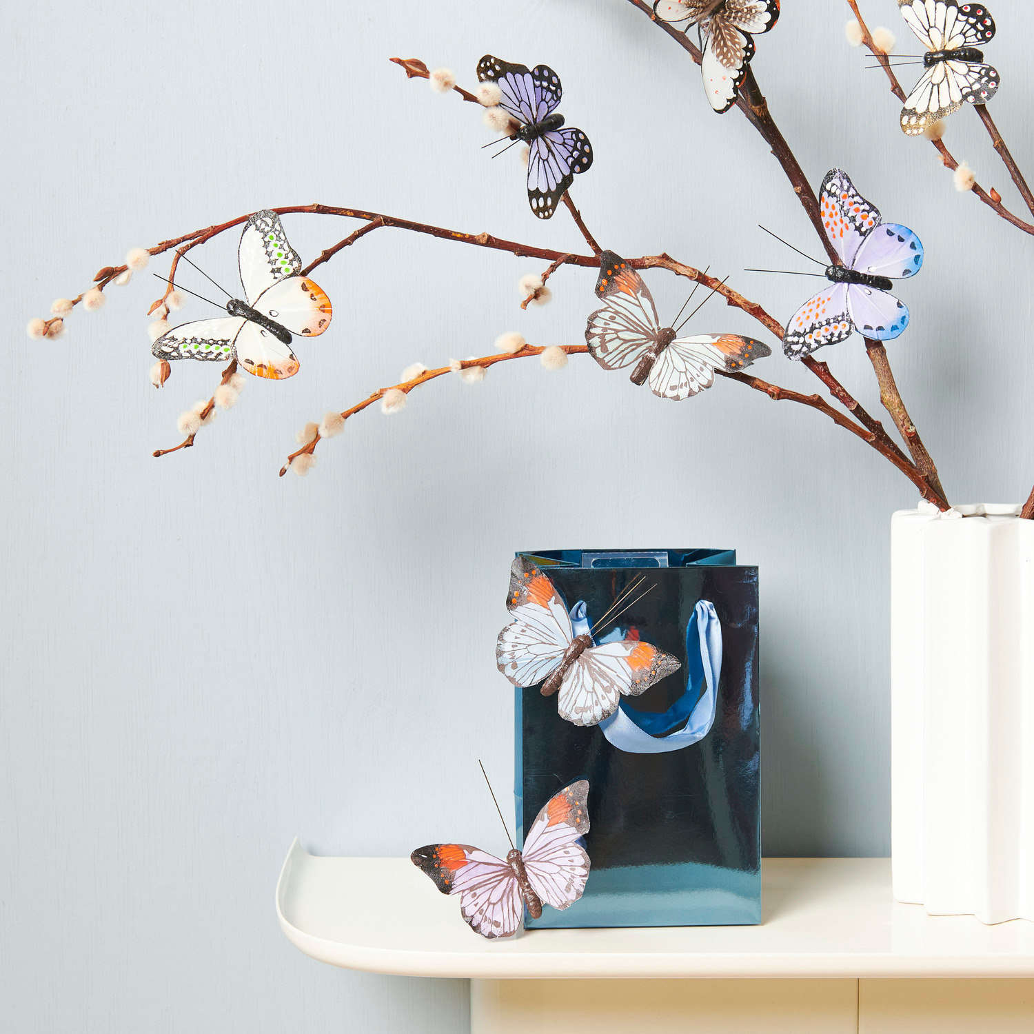 Schmetterling mit Clip Blau/Grün: Dekorative Schmetterlinge an Zweigen in einer weißen Keramikvase von Rico Design.