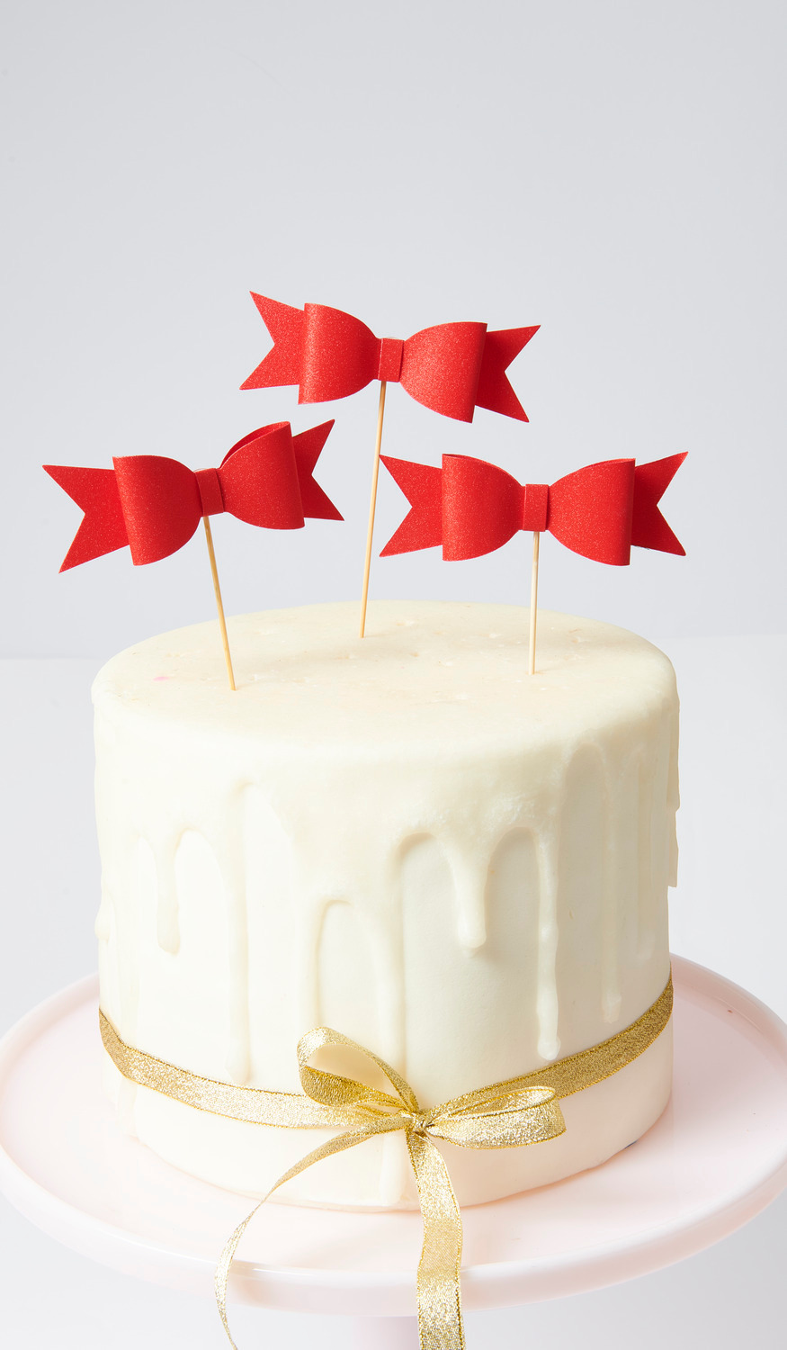 Picker Schleife Rot: Drei rote Schleifen-Picker auf einer weißen Torte mit goldener Schleife dekoriert.