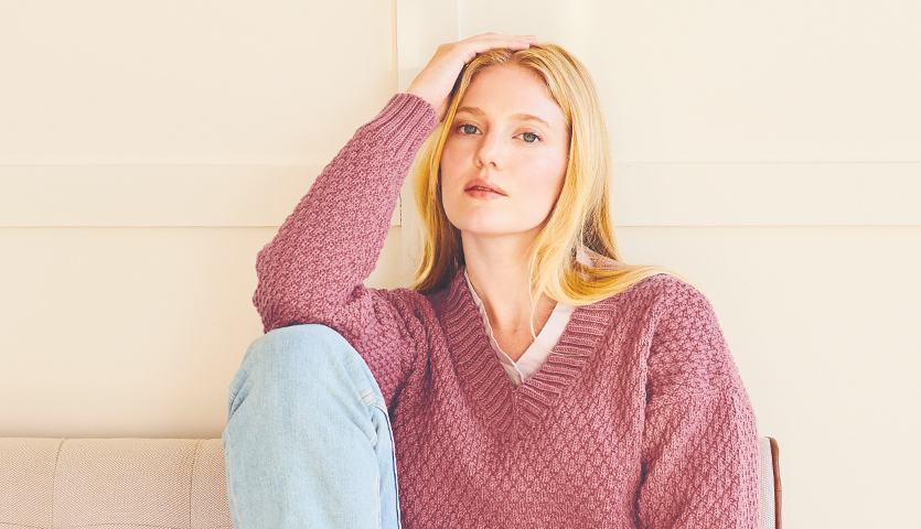 Strickanleitung Pullover aus Essentials Merino dk: Frau in rosa Pullover sitzt entspannt auf Sofa.