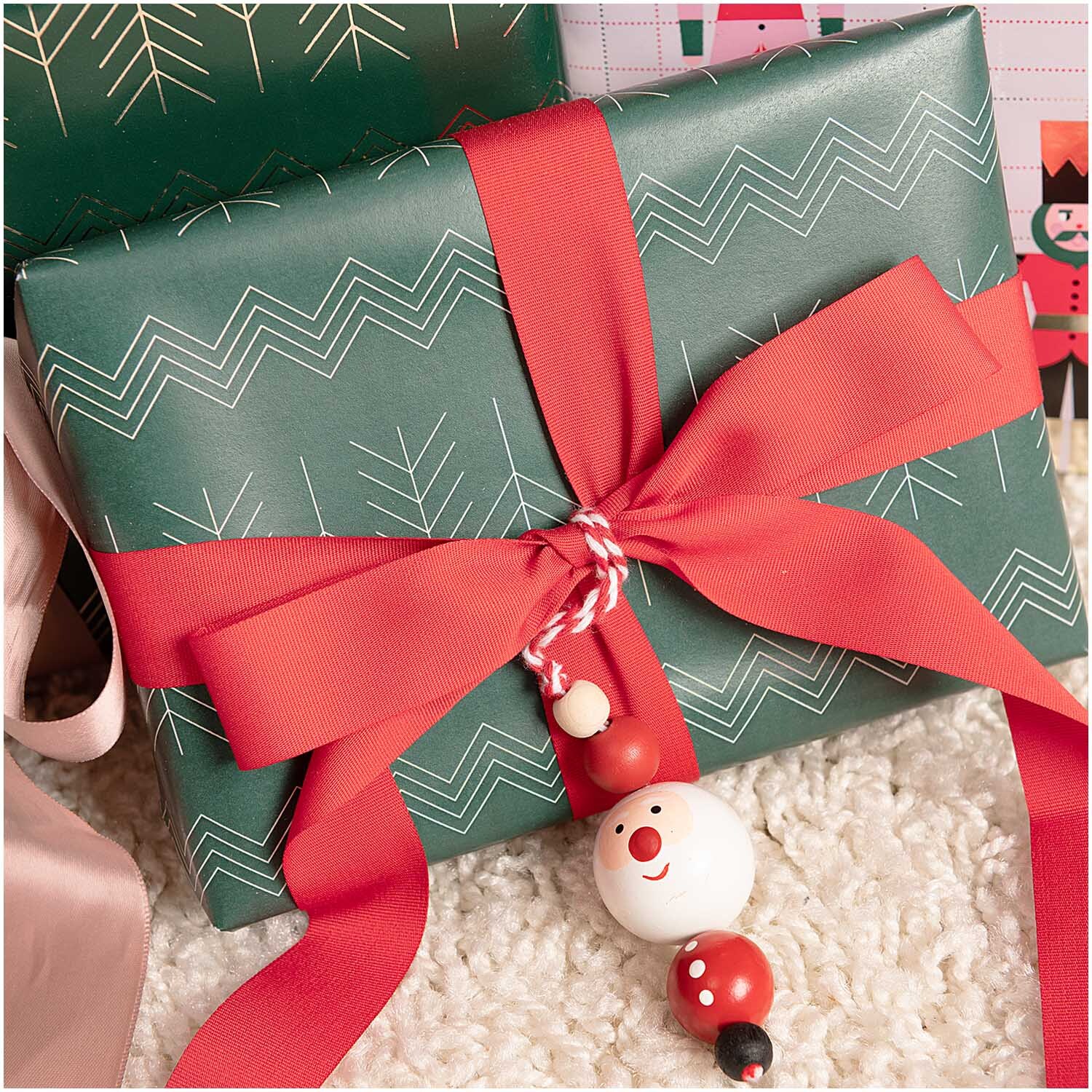 Holzhänger Santa aus Holzkugeln schmückt ein Geschenk mit rotem Band, ideal für festliche Dekorationen.