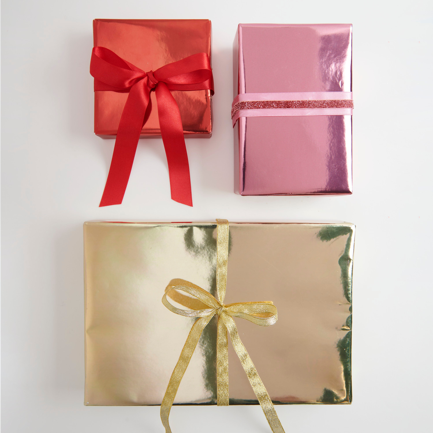 Geschenkpapier Metallic: Drei glänzende Geschenke in Gold, Rot und Pink mit Satinband verziert.