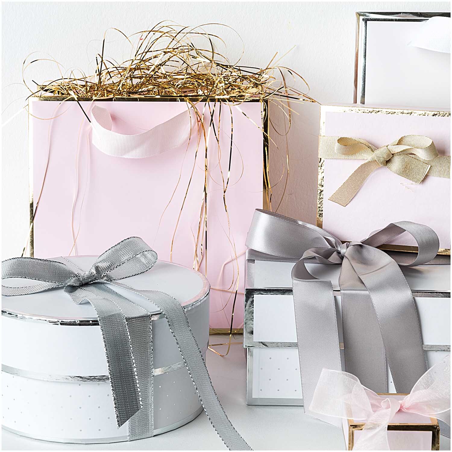 Paper Poetry Geschenkschachtel rund weiß mit silbernem Band, umgeben von eleganten Geschenkboxen in Pastelltönen und Schleifen.