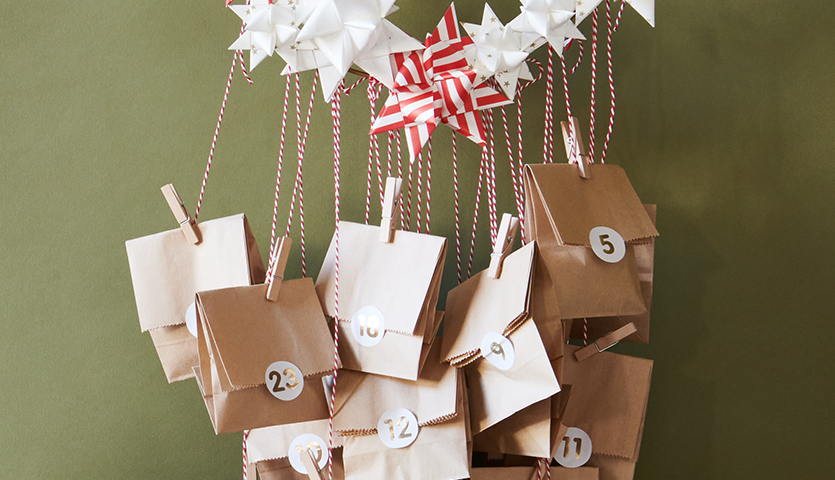 Bastelanleitung Papiertüten-Adventskalender mit Fröbelsternen: Braune Tüten mit Zahlen, dekoriert mit weißen und roten Fröbelsternen an Schnüren.