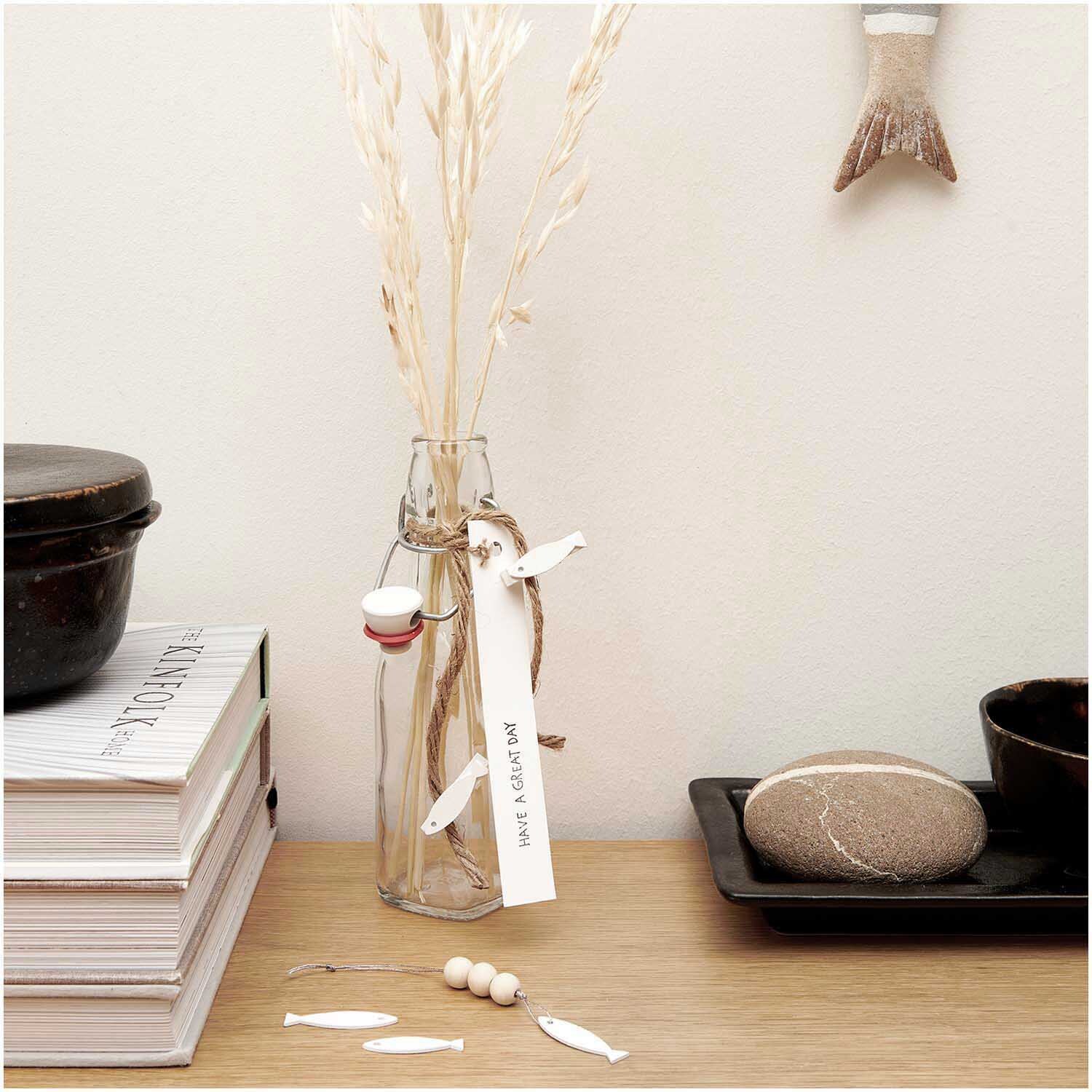 Dekoklammern Fisch weiß 7x35mm 8 Stück von Rico Design neben einer Vase mit Gräsern auf einem Tisch.