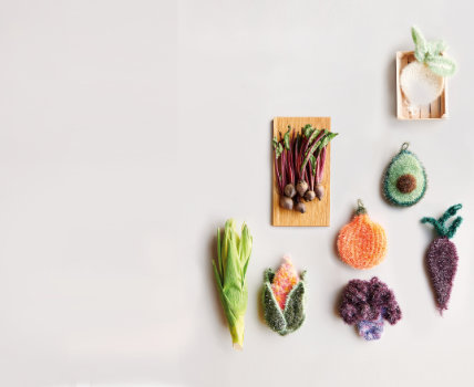 Gehäkelte Schwämme in Avocado-, Blumenkohl-, Kürbis-, Rote Beete- und Maisform, sowie echtes Gemüse. Flatlay von Produkten. 