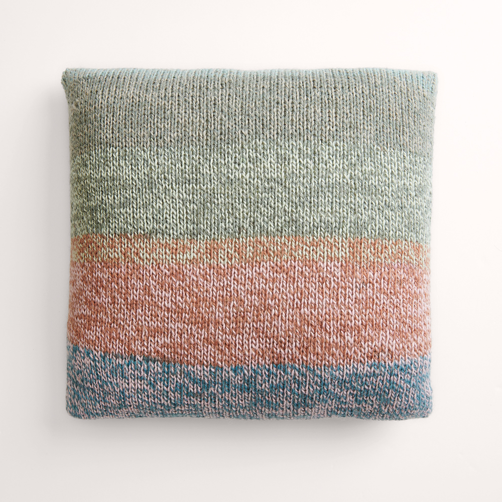 Buntes Kissen auf grauem Hintergrund – zum Strickset