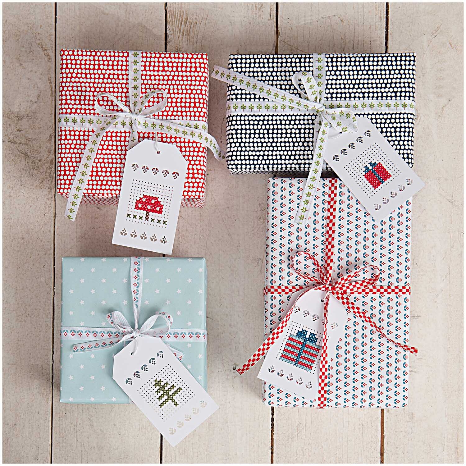 Anhänger zum Besticken creme 24 Stück von Rico Design auf Geschenken mit verschiedenen Mustern und Schleifen.