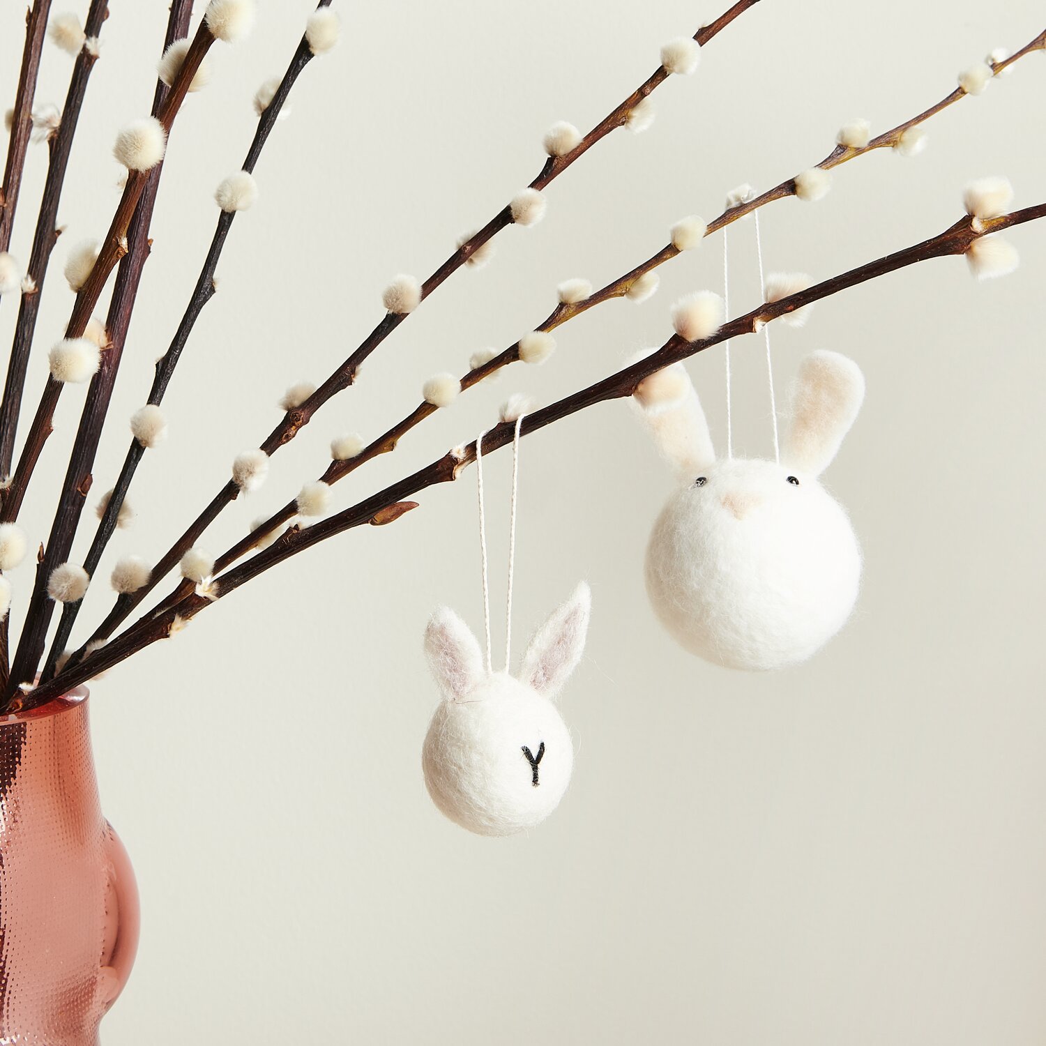 Aufhänger Filz-Hasenkopf Weiß: Zwei weiße Filz-Hasenköpfe von Rico Design hängen an Zweigen in einer Vase.