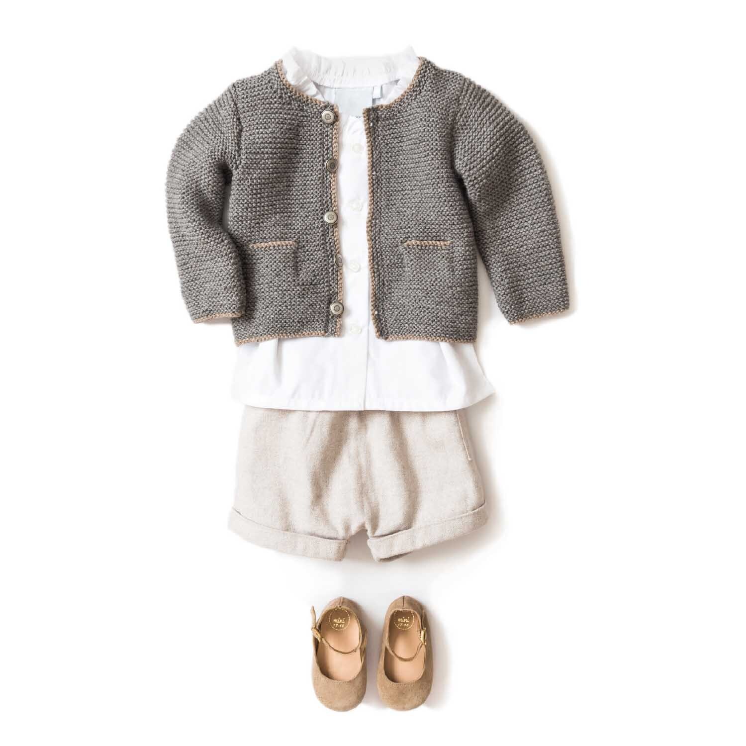Essentials Merino Plus dk: Kinderoutfit mit grauer Strickjacke, weißem Hemd, beigen Shorts und passenden Schuhen. Ideal für stilvolle Anlässe.