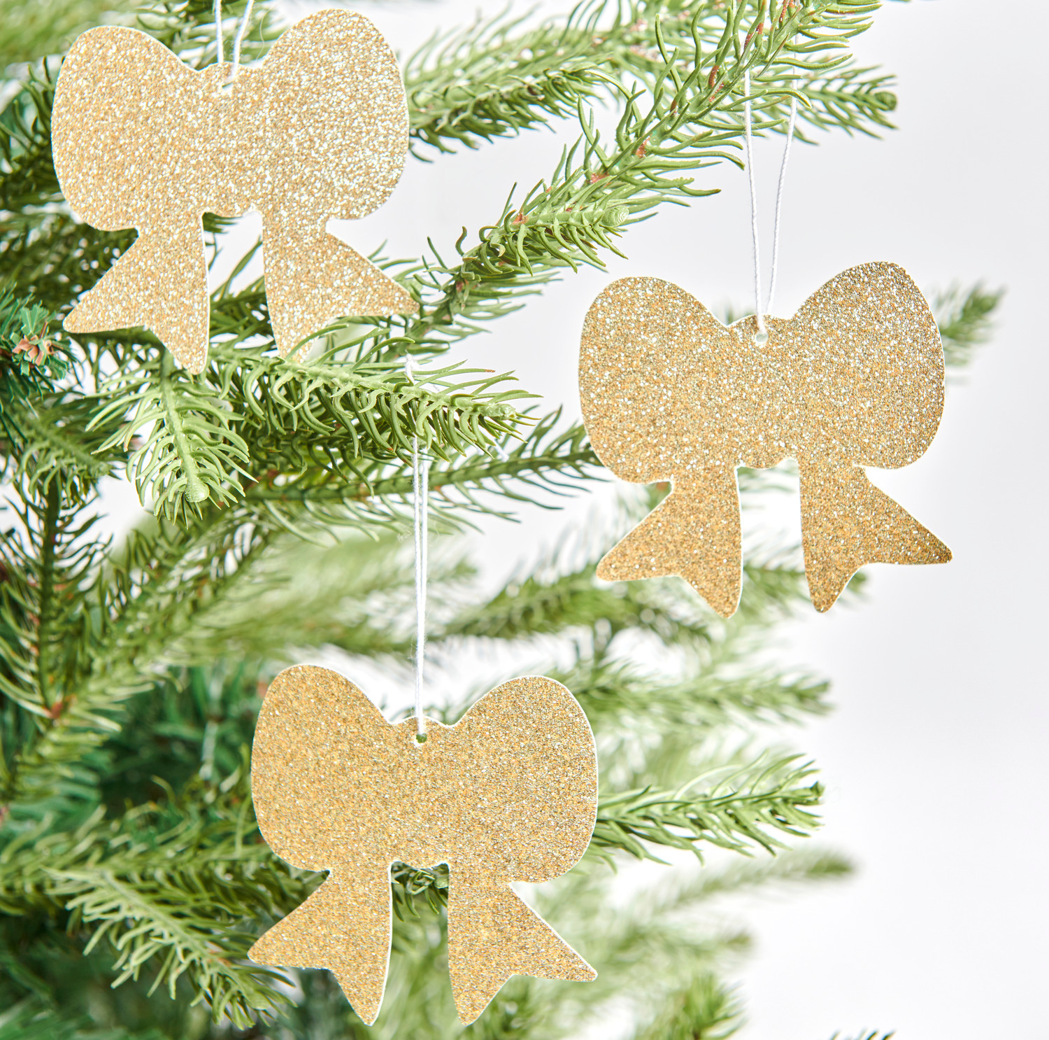 Paper Poetry Motivpapierblock Put a Bow on It: Goldene Schleifen-Anhänger schmücken einen Tannenbaum. Perfekt für festliche Dekorationen.