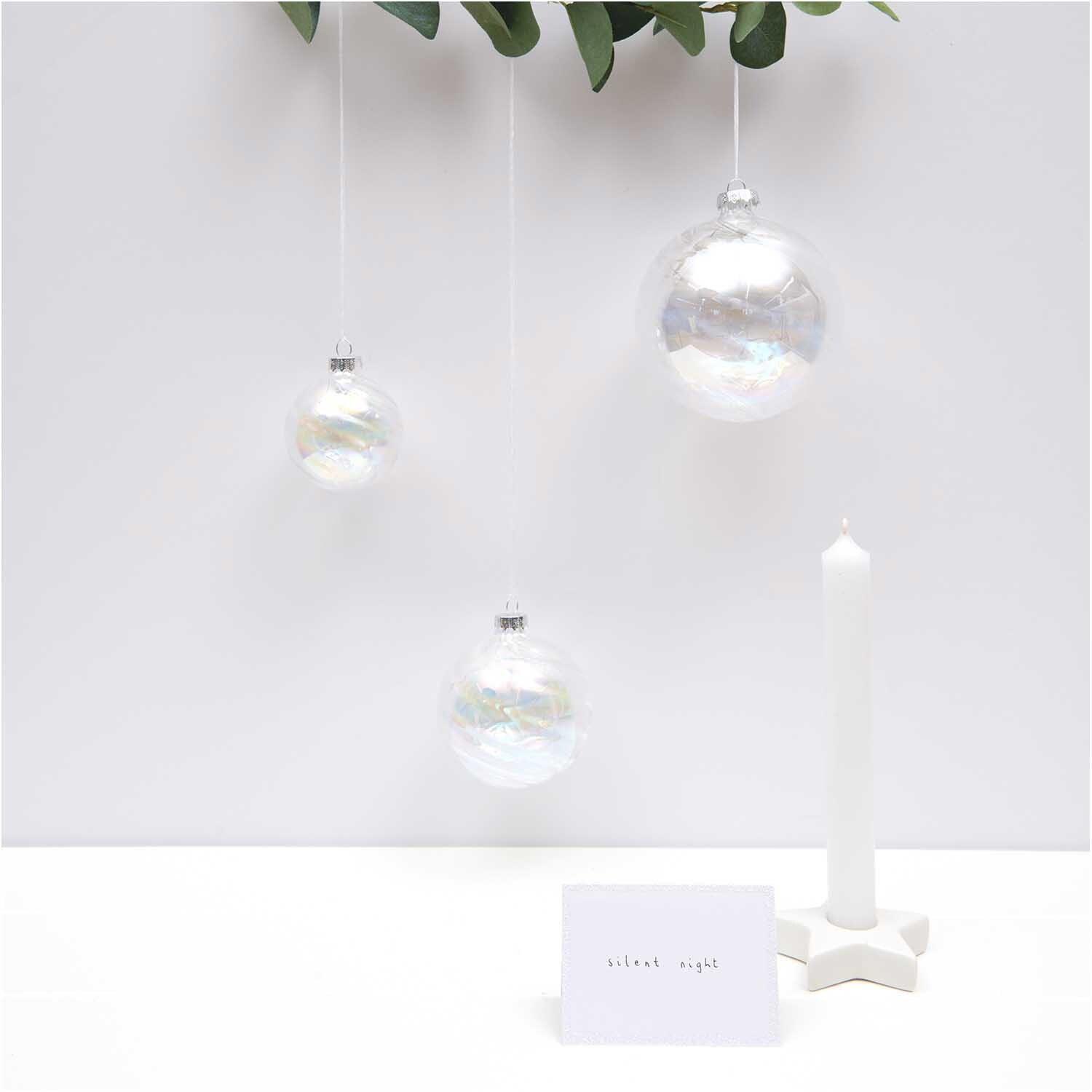 Paper Poetry Tischkarten in elegantem Weiß-Glitter, dekoriert neben schwebenden Glaskugeln und einer Kerze. Ideal für festliche Anlässe.