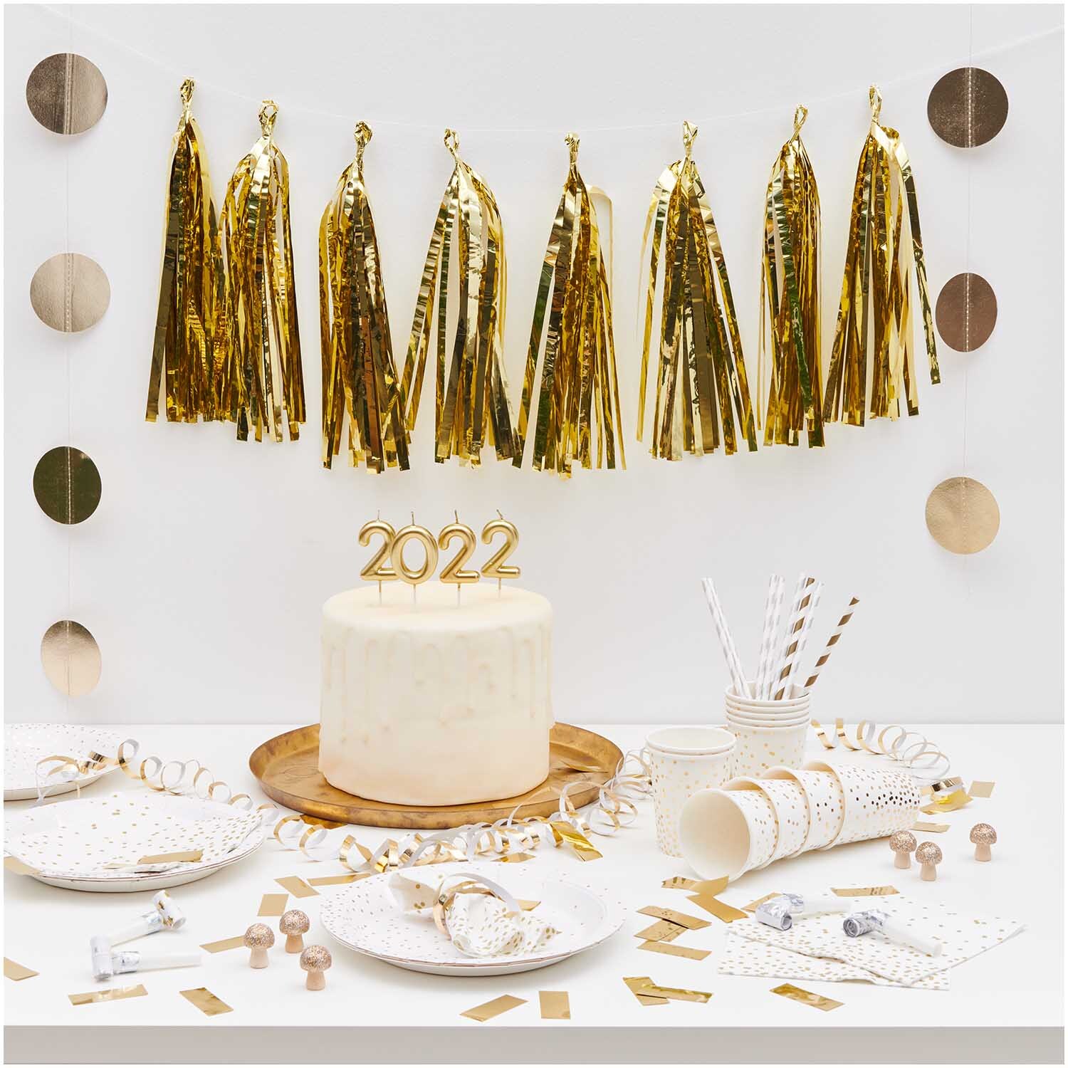 Genähte Girlande Kreise 8cm gold 1,7m von Rico Design dekoriert einen festlichen Tisch mit goldenen Akzenten und einer Torte mit der Zahl 2022.