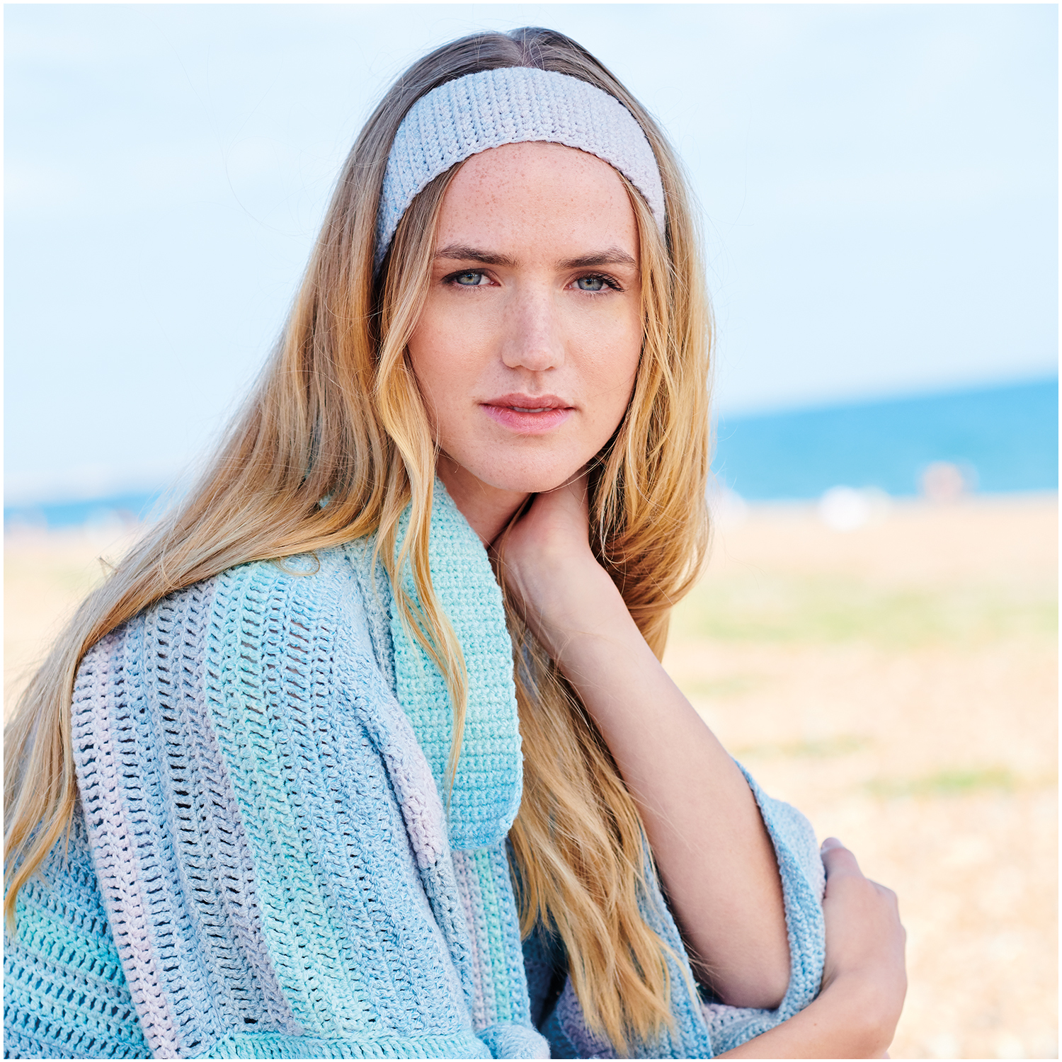 Häkelset Kimono-Jacke Modell 29: Frau am Strand in pastellfarbener Strickjacke mit Stirnband.