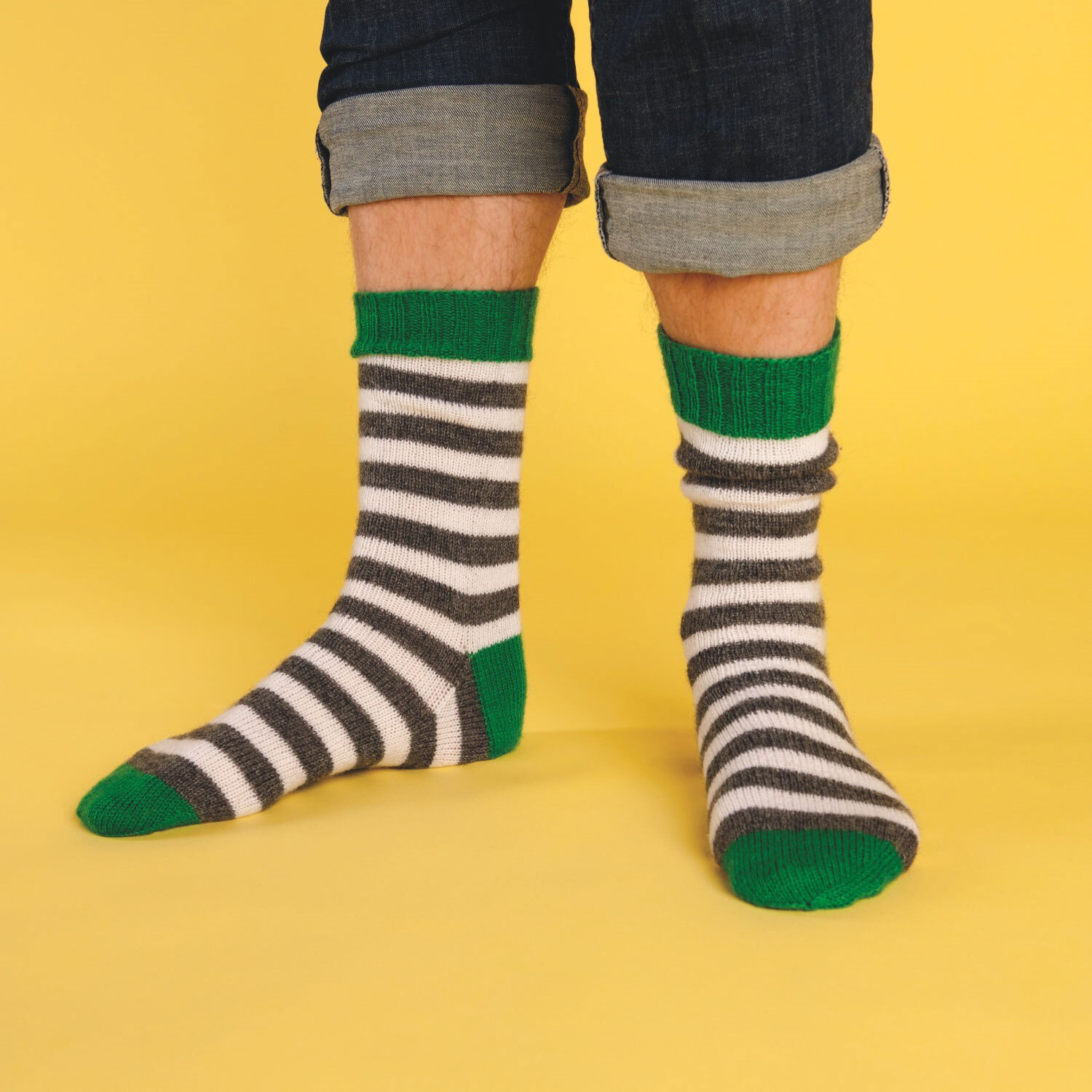 Füße tragen gestrickte Ringelsocken aus schwarzem, weißem und grünem Garn. Fotosetting gelber Hintergrund.