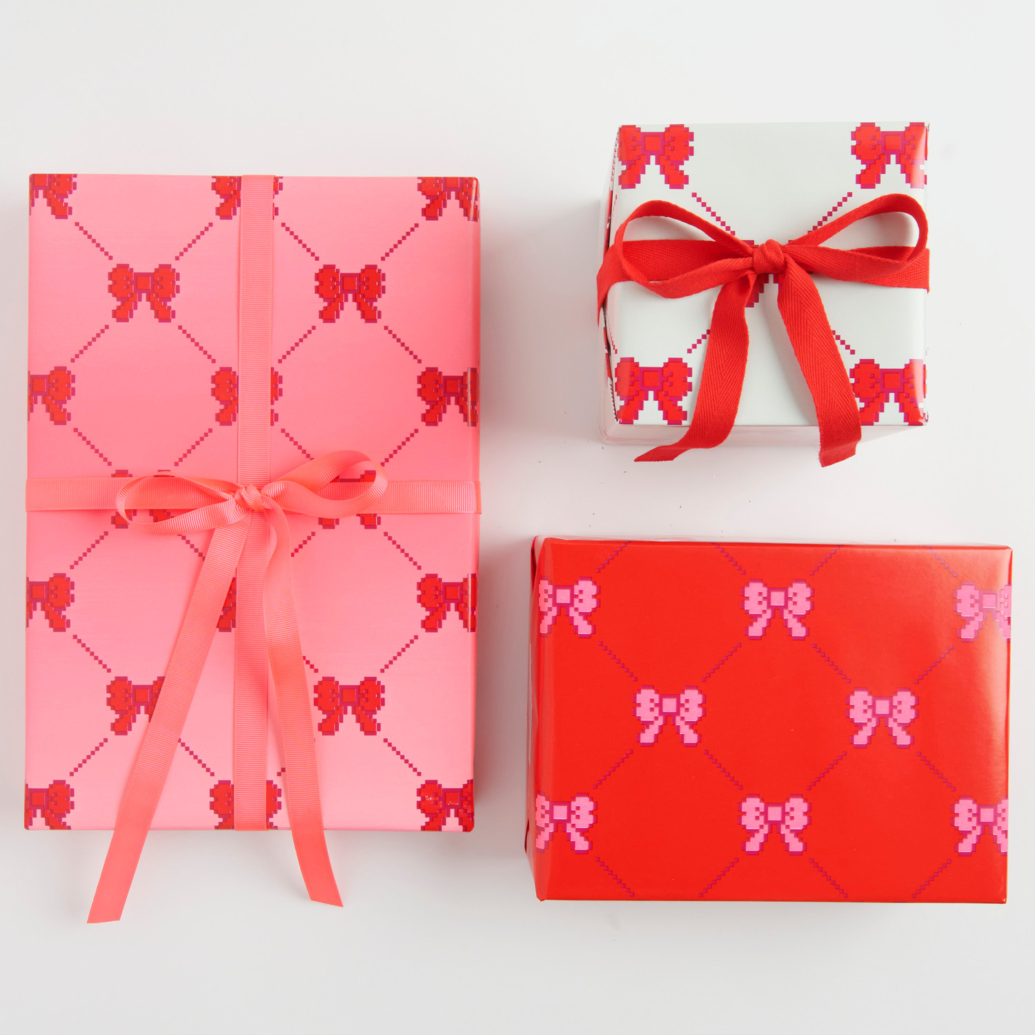 Geschenkpapier Pixel Schleifen: Drei Geschenke in Neonpink, Rot und Creme mit Schleifenmuster.