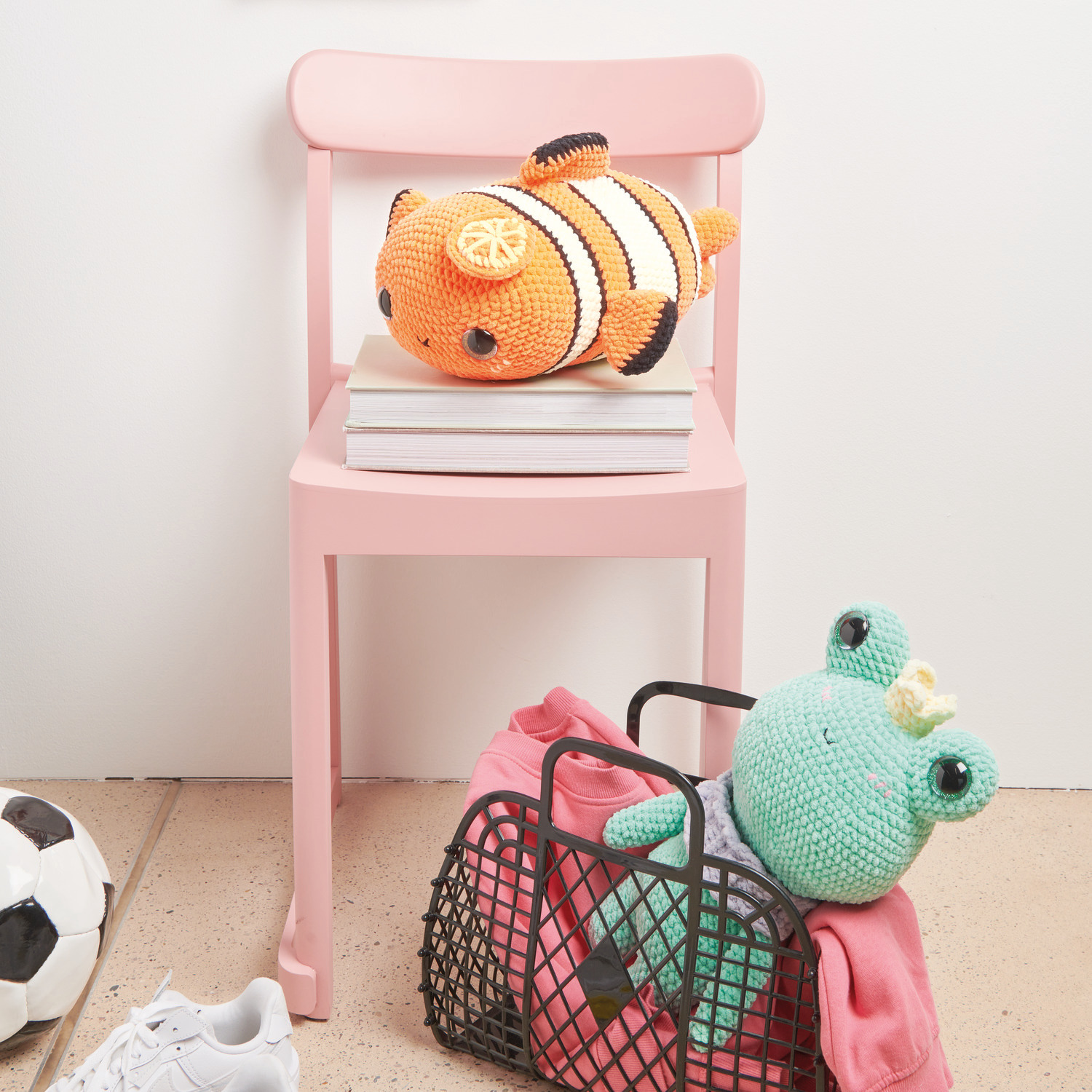 Häkelset Crazy Clown Fish Modell 04: Ein orange-weißer Clownfisch auf einem rosa Stuhl, daneben ein gehäkelter Frosch mit Krone in einem Korb.