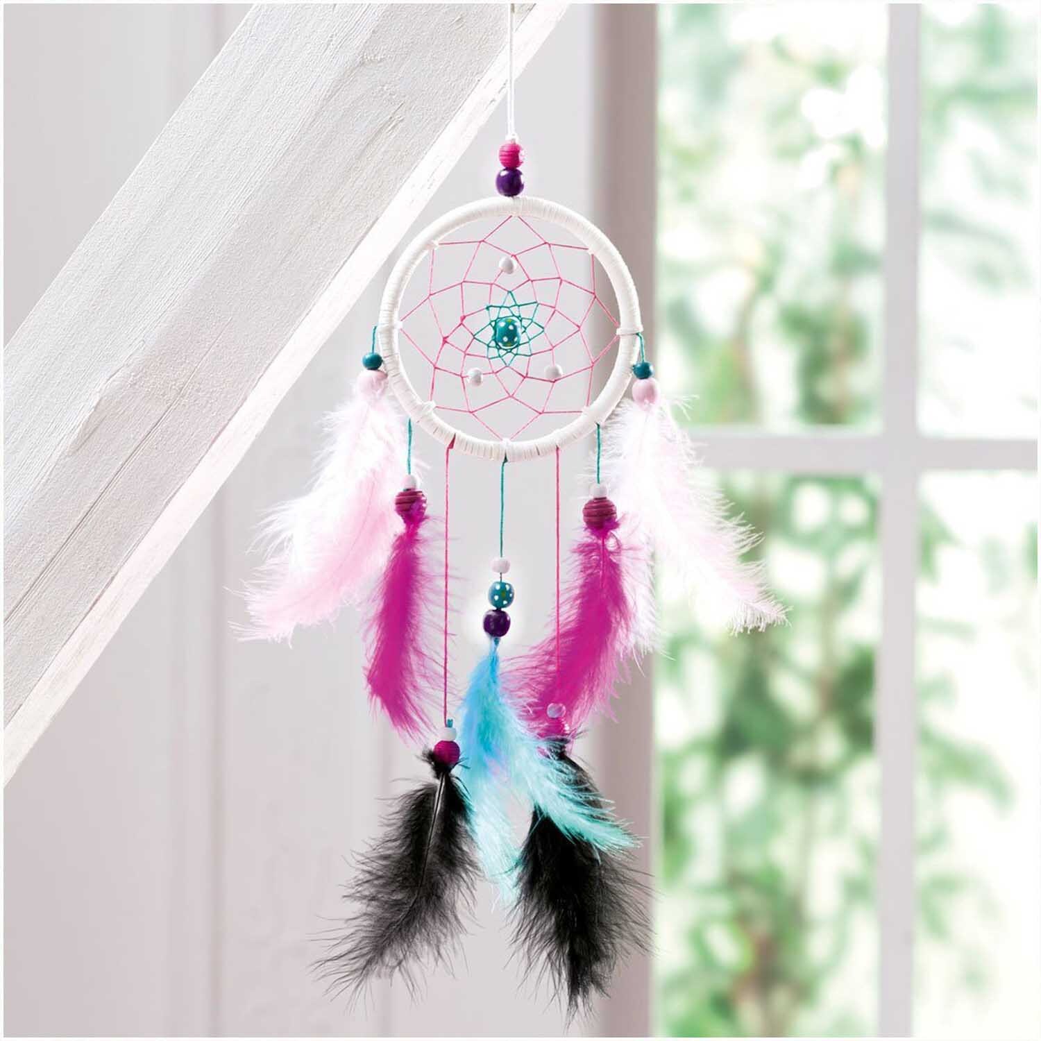 Bastelset Traumfänger Girly von folia: Ein bunter Traumfänger mit rosa, blauen und schwarzen Federn hängt vor einem Fenster.