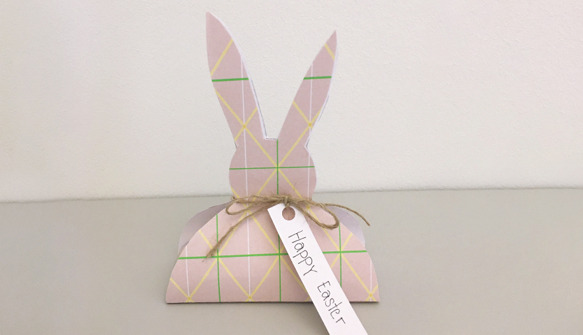 Bastelanleitung Osterhase aus Motivpapier: Ein pastellfarbener Papierhase mit geometrischem Muster und "Happy Easter"-Schild.
