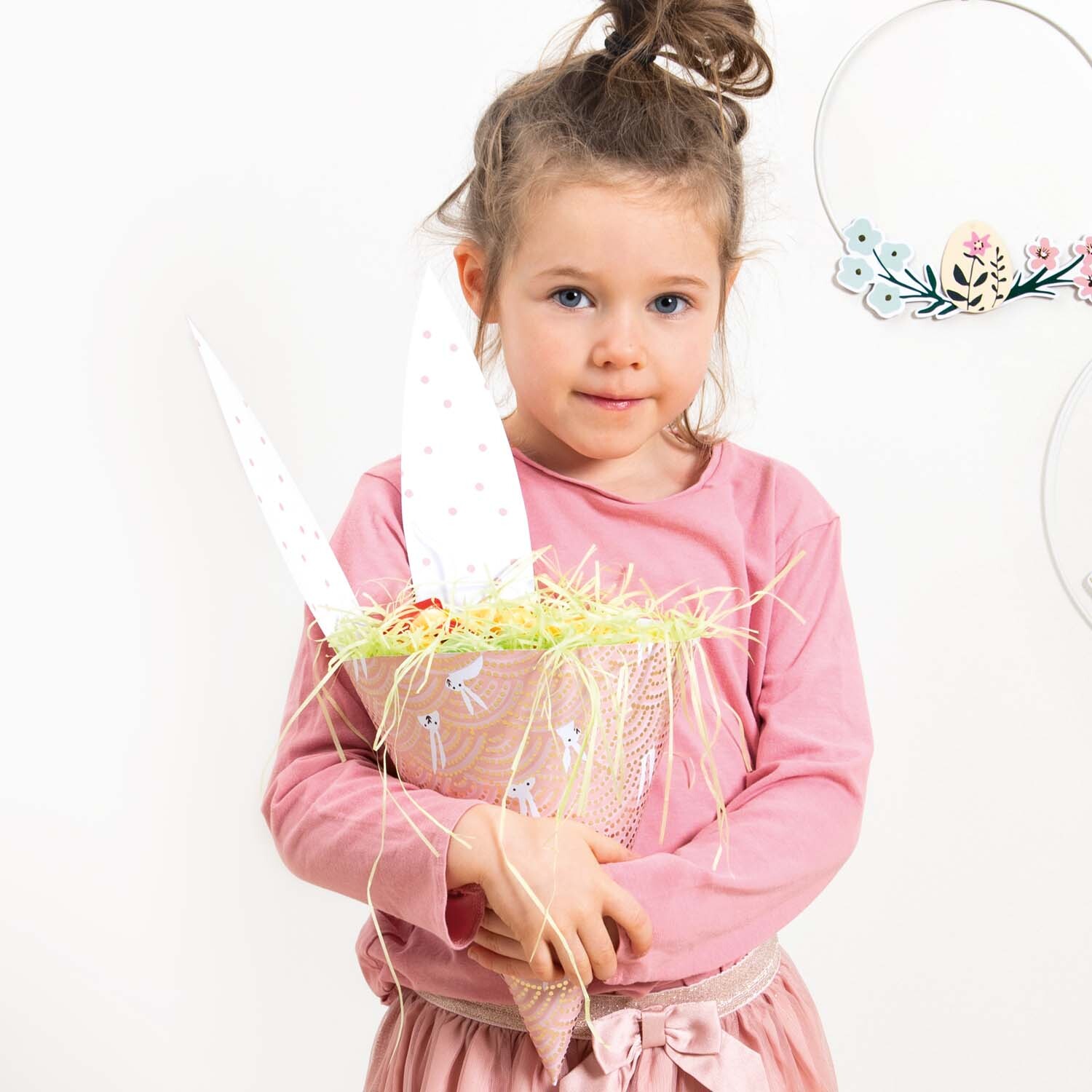 Bastelanleitung Hasengeschenktüte: Mädchen in rosa Kleid hält eine dekorative Hasengeschenktüte mit Ohren.