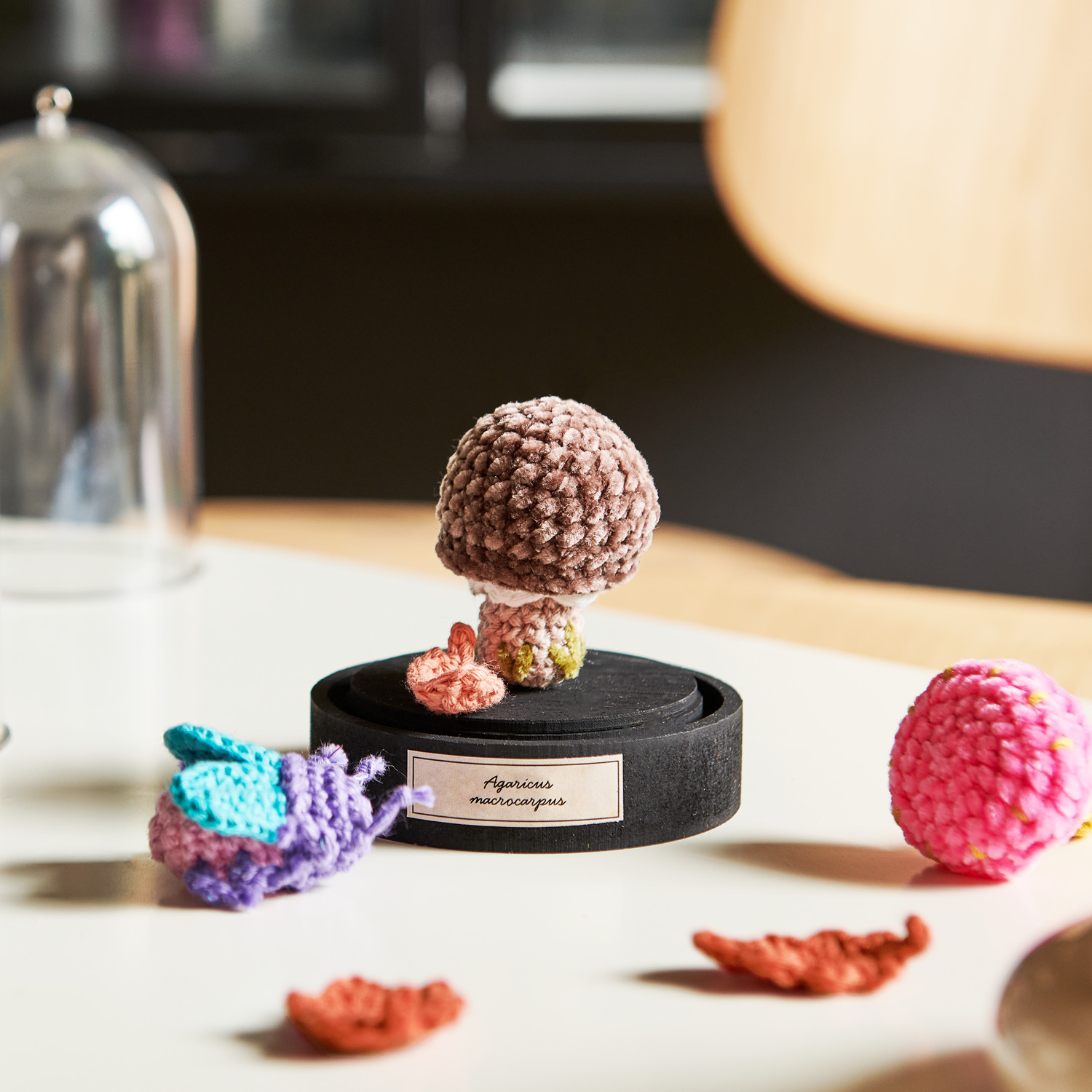 Ricorumi Twinkly Twinkly dk, gehäkelter Pilz in Schokolade auf schwarzem Sockel, umgeben von bunten Garnfiguren.