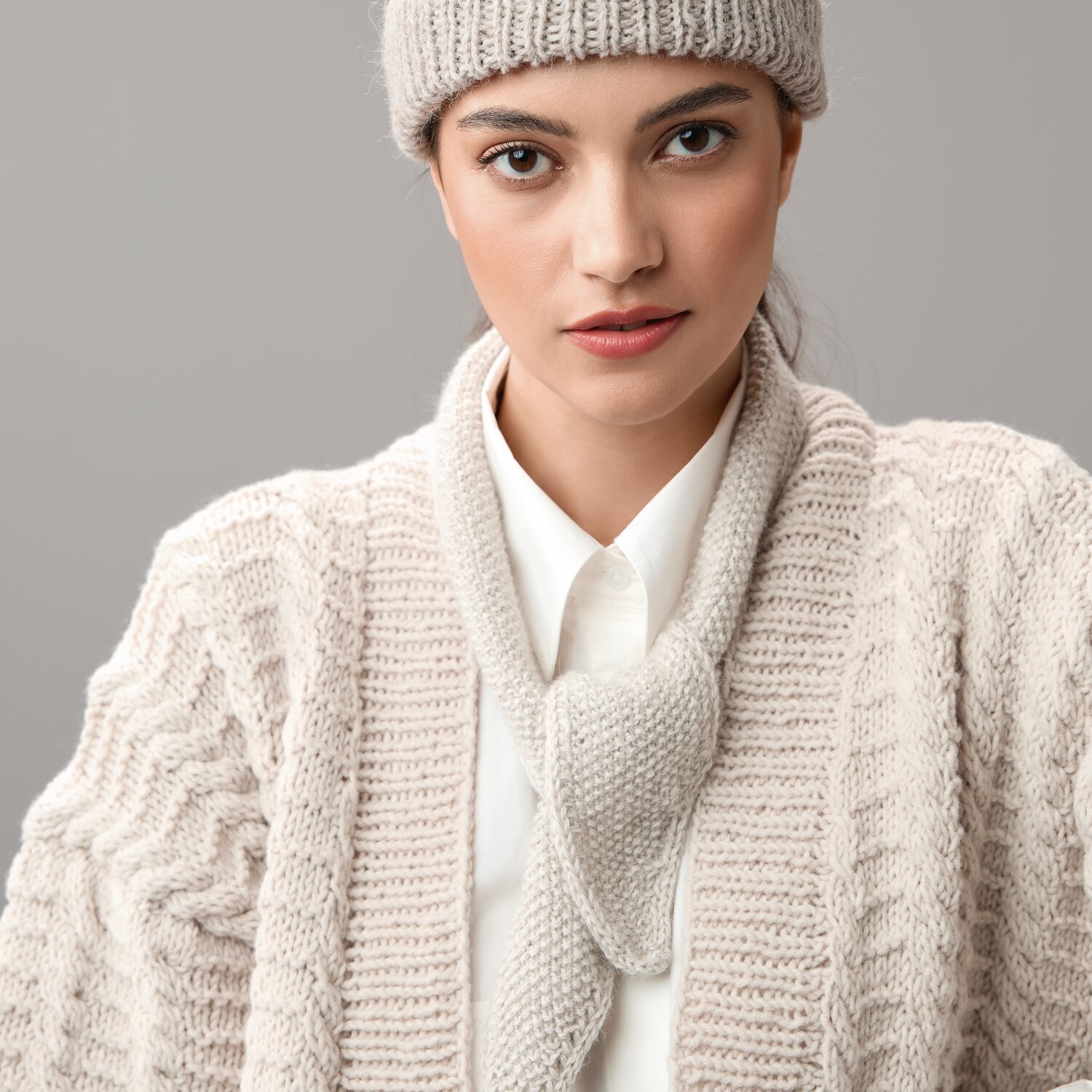 Strickset Mini-Tuch Modell 04: Frau trägt cremefarbenes Strickset mit Mütze und Schal. Ideal für kühle Tage.