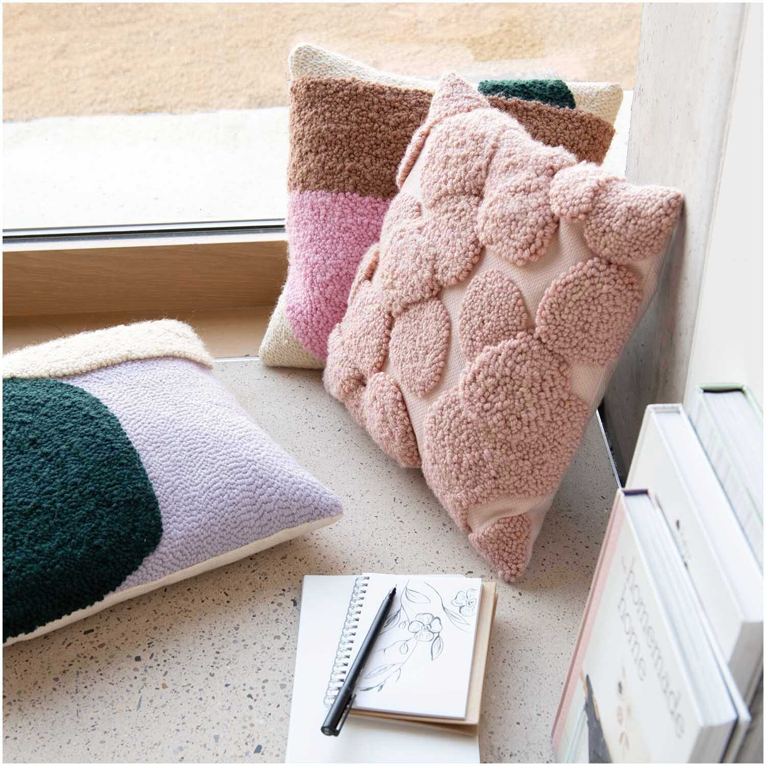 Punch Needle Packung Kissen mit rosa Punkten von Rico Design auf einem Fensterbrett arrangiert.