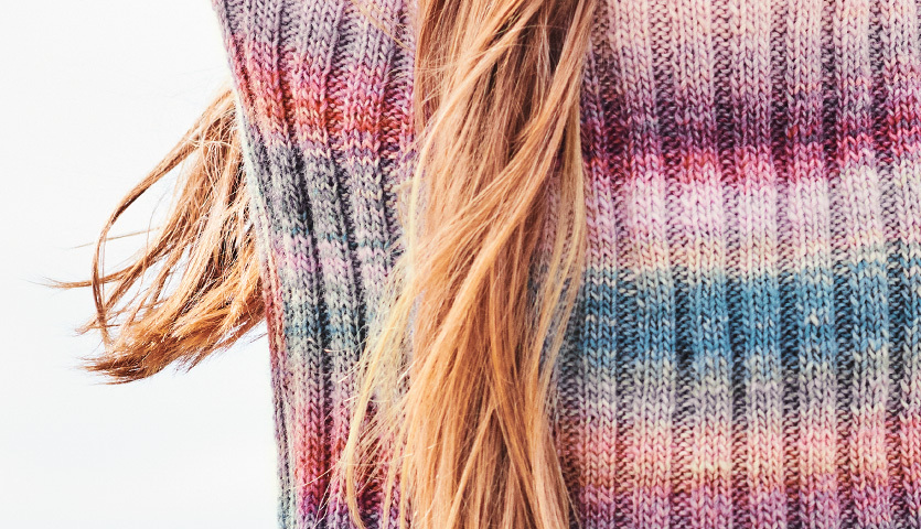 Strickanleitung Kinderpullover mit Farbverlauf: Nahaufnahme eines bunten Strickpullovers mit langen Haaren im Bild.