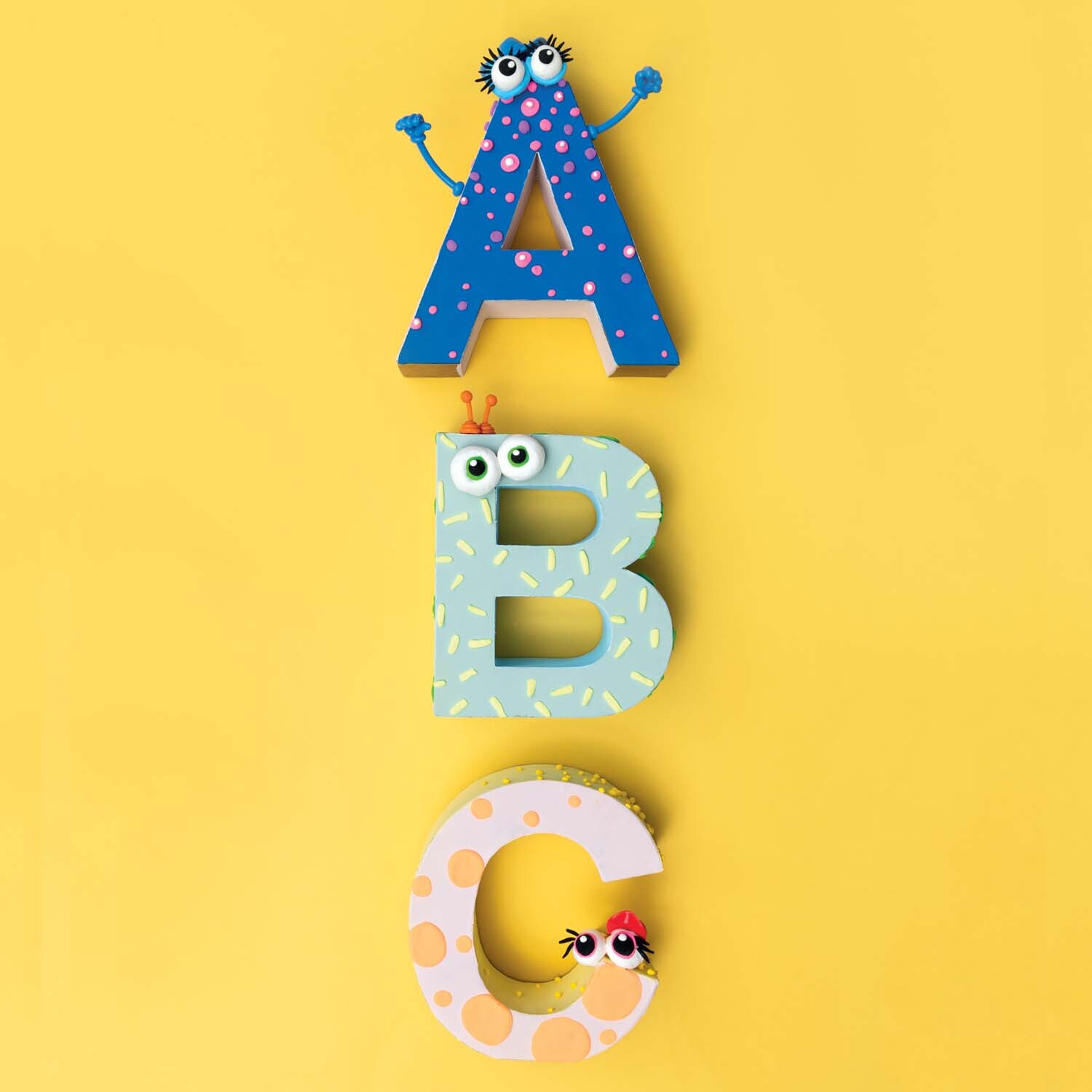 Bastelanleitung Pappbuchstaben mit Super Fluffy: Bunte Buchstaben A, B, C mit Augen auf gelbem Hintergrund.