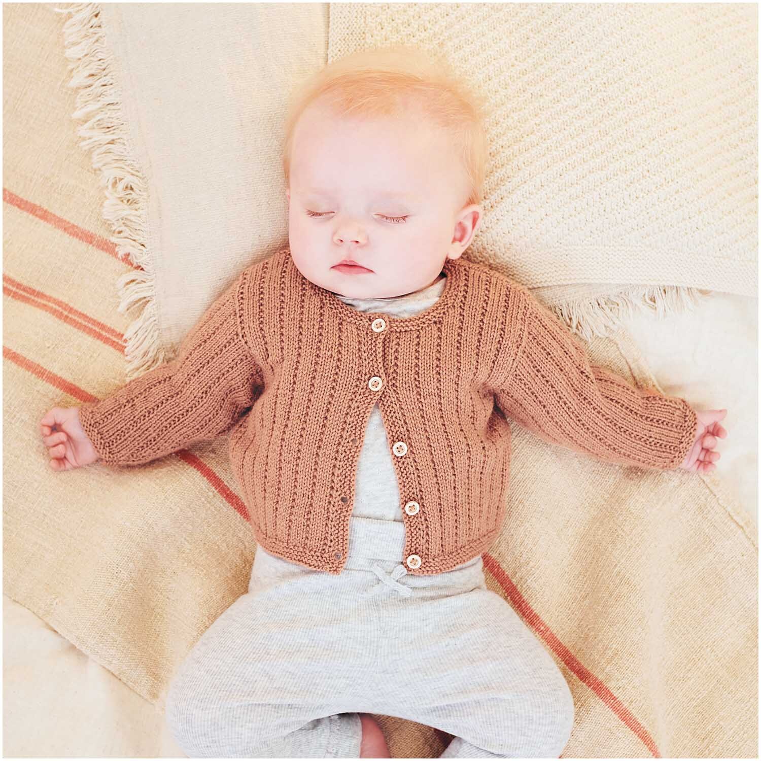 Baby Merino: Ein schlafendes Baby in einem gestrickten Cardigan aus weicher Wolle auf einer Decke.