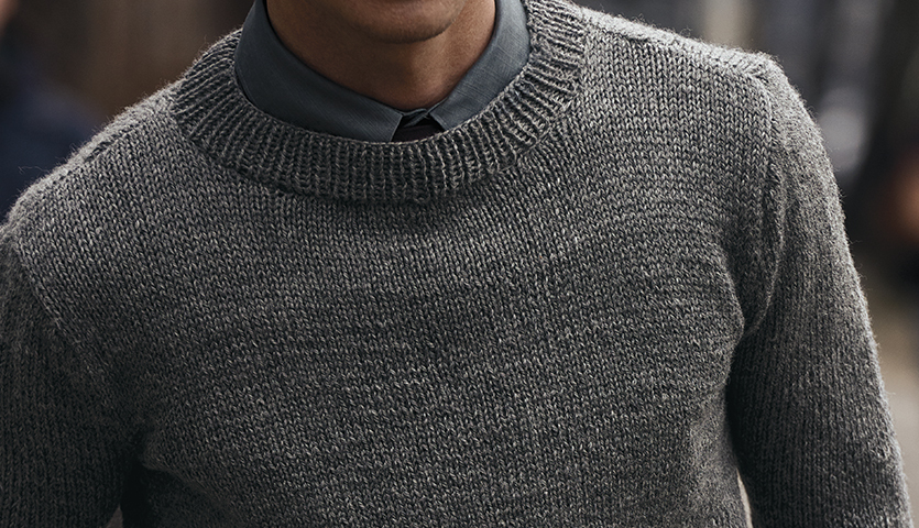 Strickanleitung Herrenpullover aus Essentials Soft Merino aran: Grauer Pullover aus weicher Merinowolle, getragen von einem Mann mit Hemd.