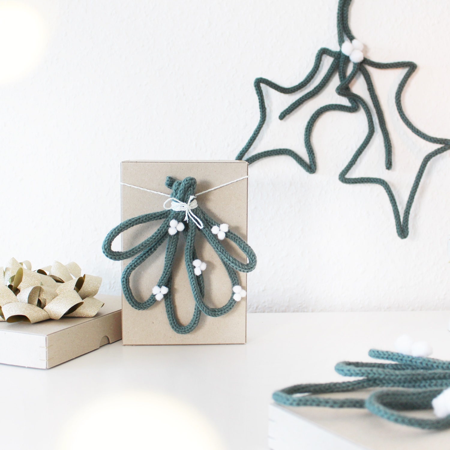 Inspiration DIY Mistelzweig mit der Strickmühle @tinkerhome: Kreative Deko in Grün mit weißen Akzenten auf Geschenkbox.