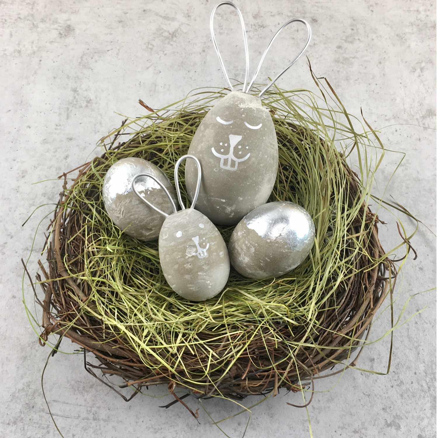 Bastelanleitung Osterhasen und Ostereier aus Beton: Betonhasen und -eier in einem Nest aus Zweigen und Gras. Ideal für kreative Osterdekorationen.