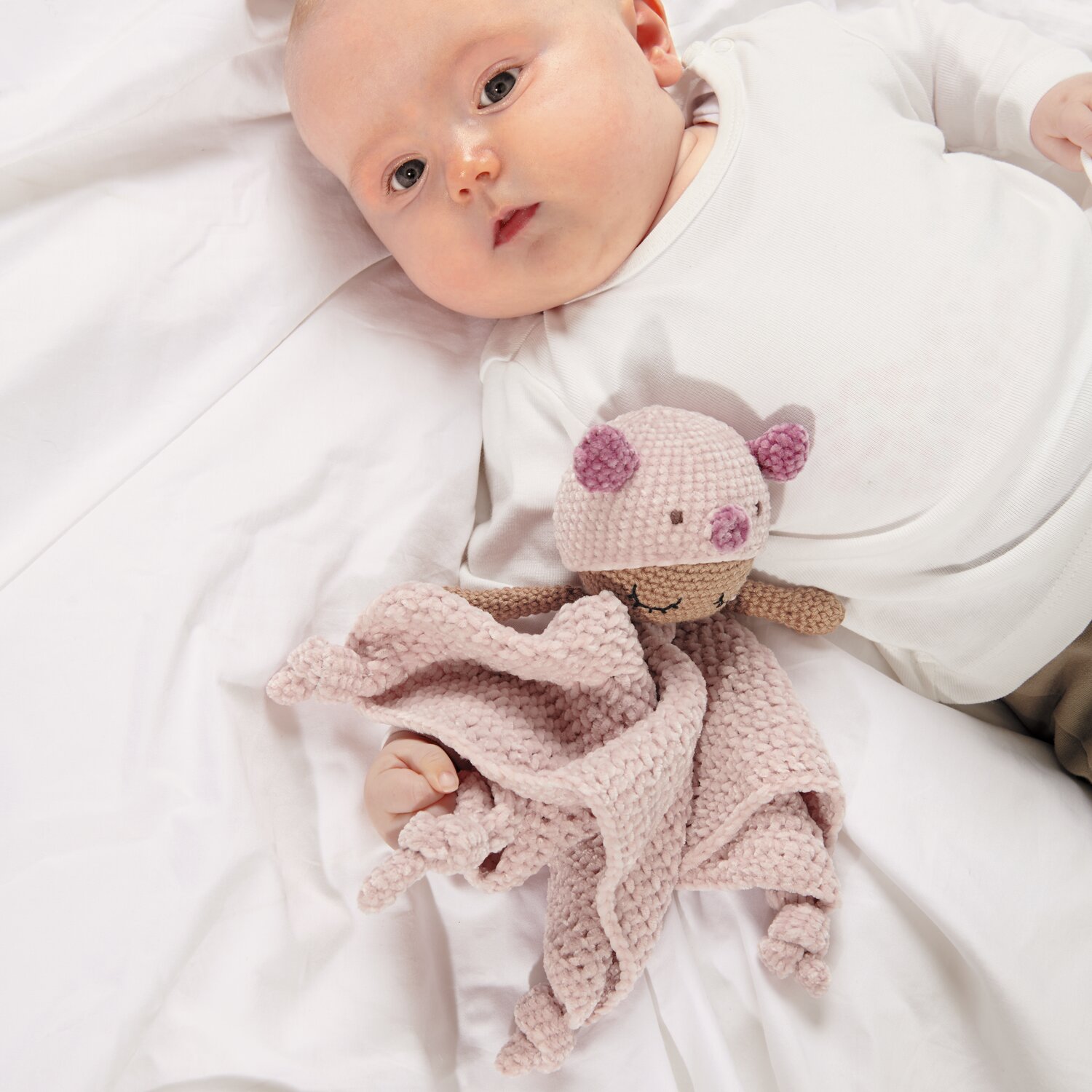 Ricorumi Baby Blankies Nilli Nilli: Ein Baby liegt auf einer Decke mit einem gestrickten Kuscheltier in zarten Farben.