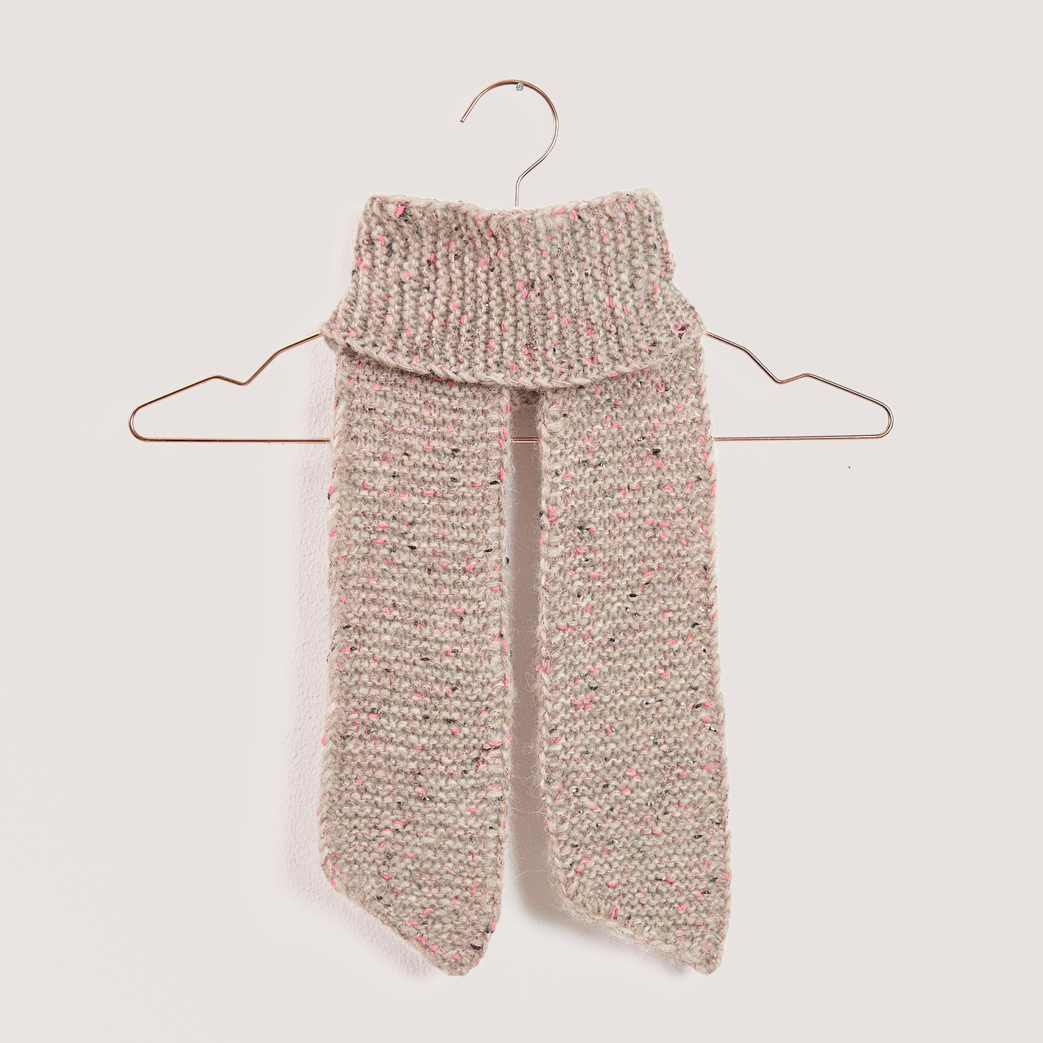Strickset Mini Schal Modell 03b: Ein gestrickter Schal in Beige von Rico Design, hängend auf einem Kleiderbügel.