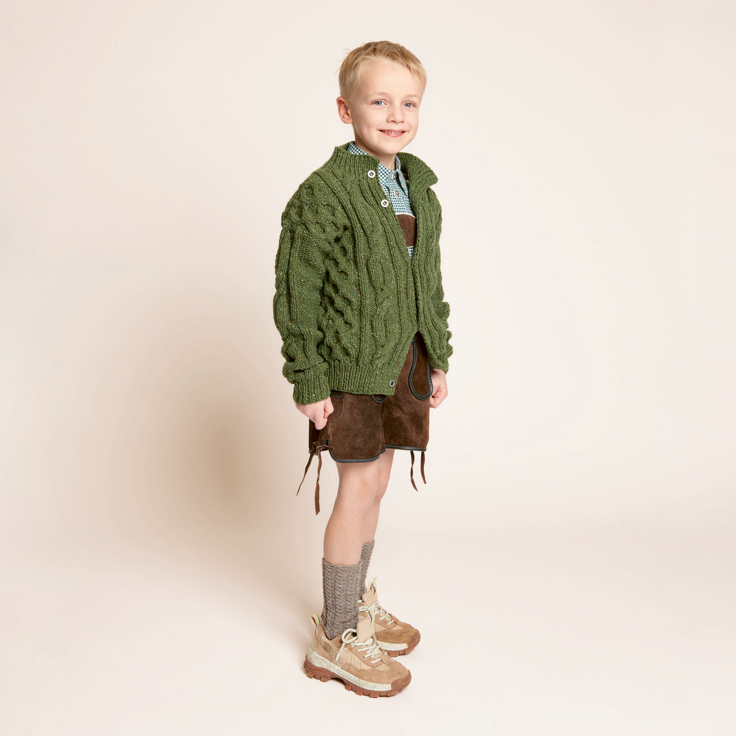 Strickset Kinderjacke Modell 24: Junge in grüner Strickjacke und Trachtenhose, lächelnd.